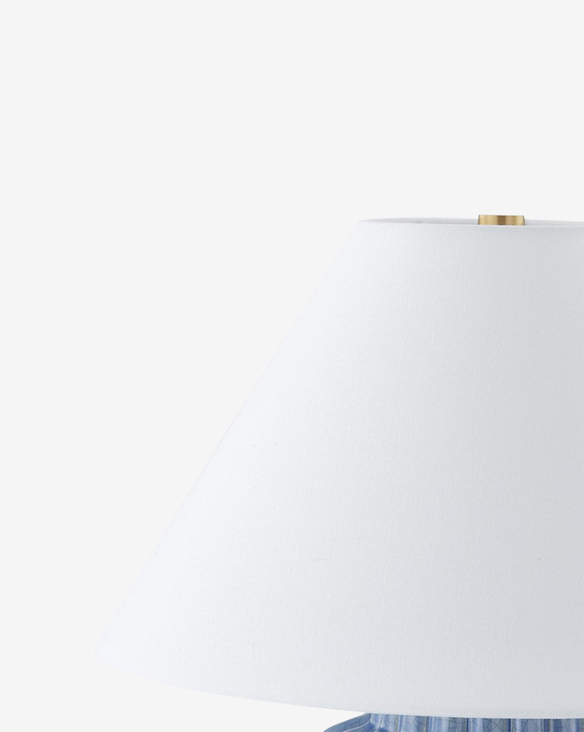 A close-up of the Clarendon Table Lamp highlights its white shade with a brass finial, set against a plain white background. The image shows the upper right side of the lamp and part of its blue ceramic base, by McGee & Co.