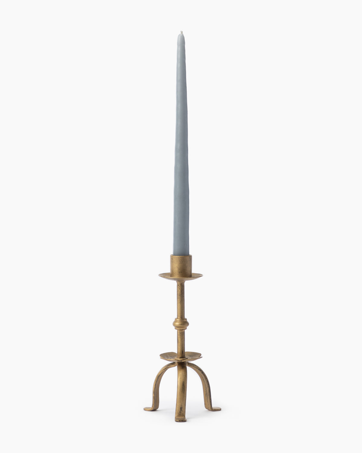 A tall, pale blue taper candle sits in the Claridge Taper Holder, an antique brass piece with three curved legs and a round base—ideal for mantel decor set against a plain white background.