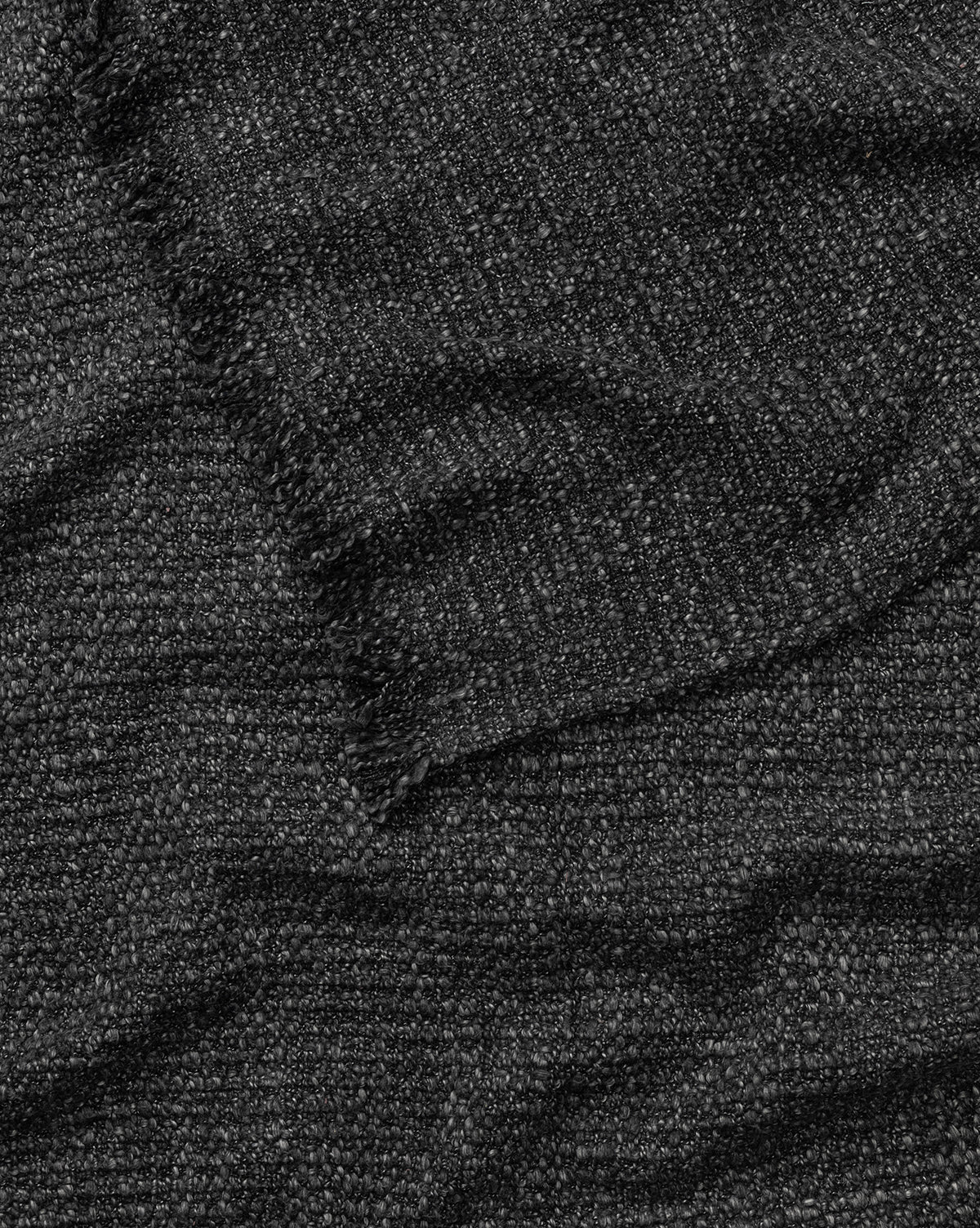 A close-up of the Clarissa Throw Blanket by Creative Co-op shows its dark, textured cotton blend fabric with visible fibers, a frayed edge, and subtle waves and folds—McGee & Co.