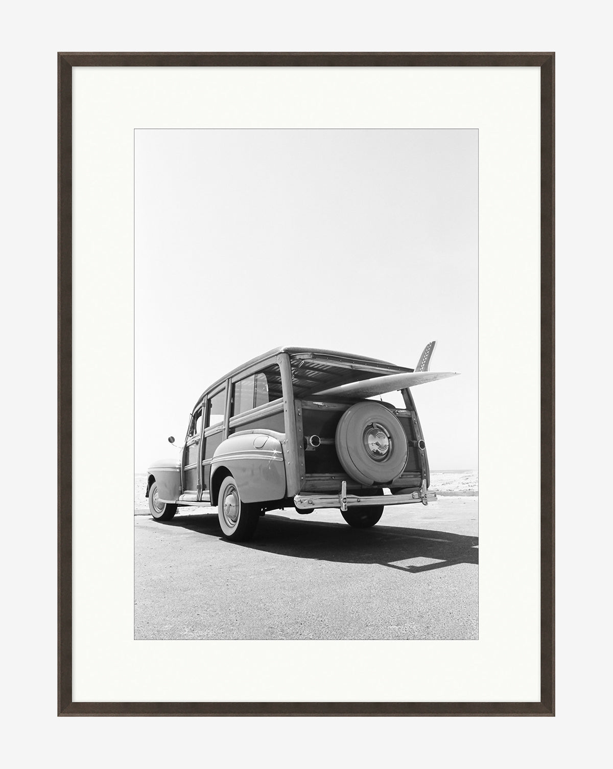 Classic Surf: Black and white giclee print of a vintage station wagon with a surfboard, parked roadside by the sea. Framed to museum standards with a white mat and dark border for timeless surf-inspired style.