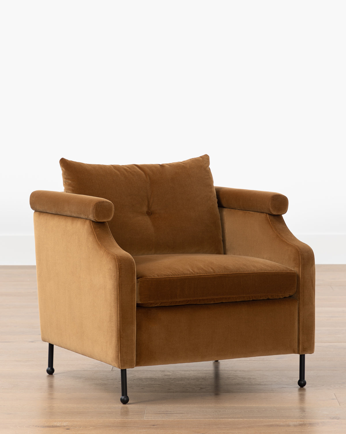 The Clegg Lounge Chair (Ready to Ship) features brown cotton velvet upholstery, rounded arms, and a cushioned backrest on sleek iron legs, displayed on a light wood floor against a white background by McGee & Co.