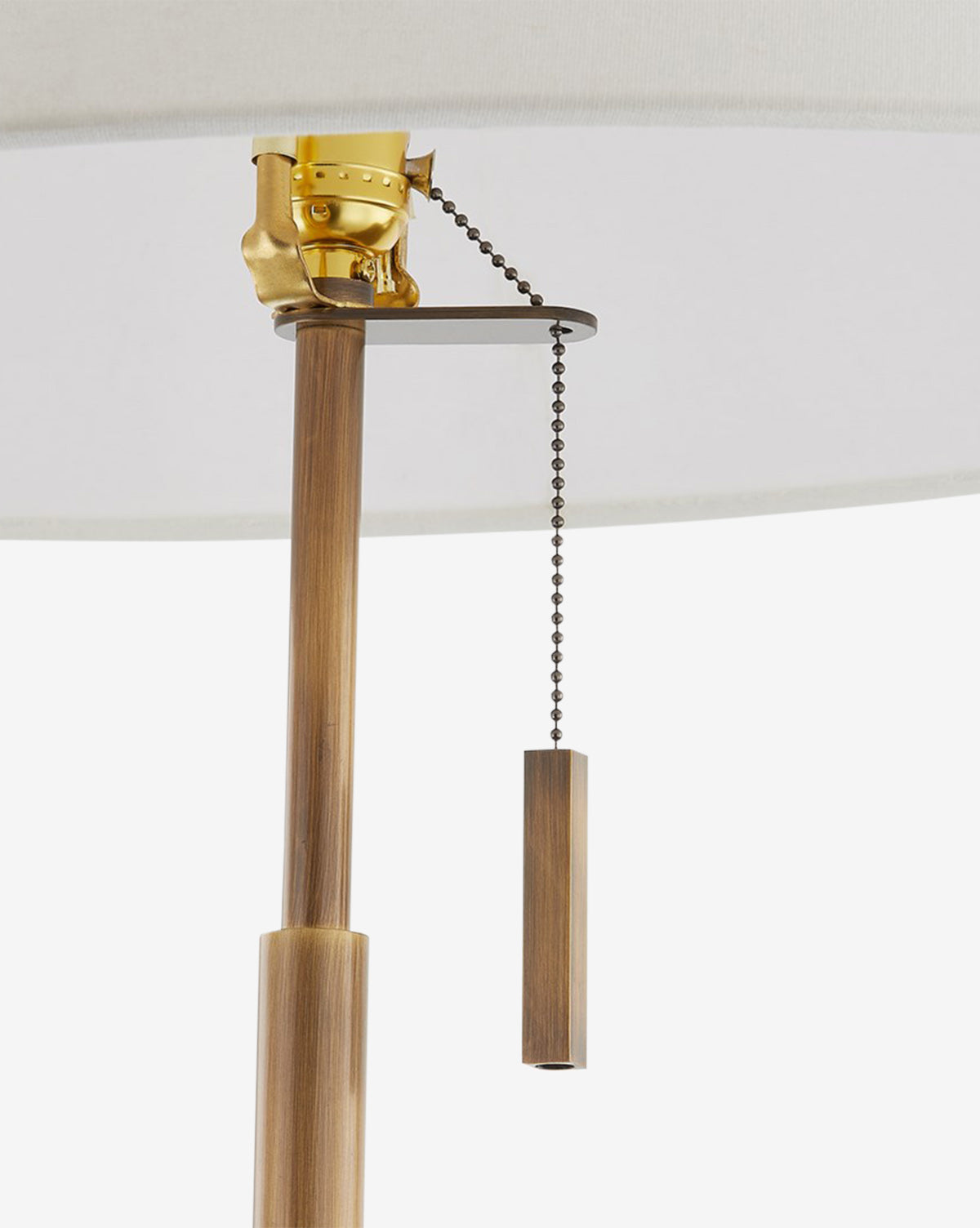 A close-up of the Clic Floor Lamp’s pull chain highlights its brass fixture, brown wooden pole, and cylindrical wooden pull beneath an off-white linen shade, by McGee & Co.