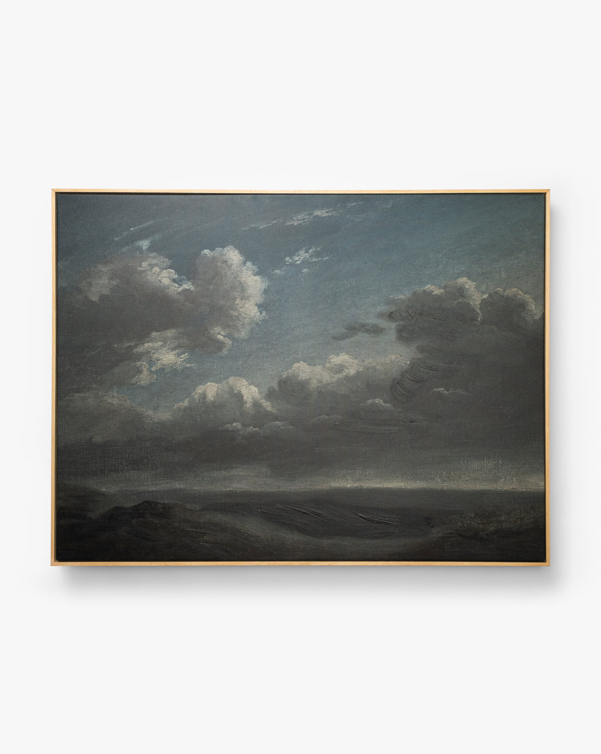 The Clouds Over Mountains framed art features a dramatic sky with dark clouds above a shadowy landscape, illuminated by a hint of light. This atmospheric wall art creates a captivating and moody focal point for any room by McGee & Co.