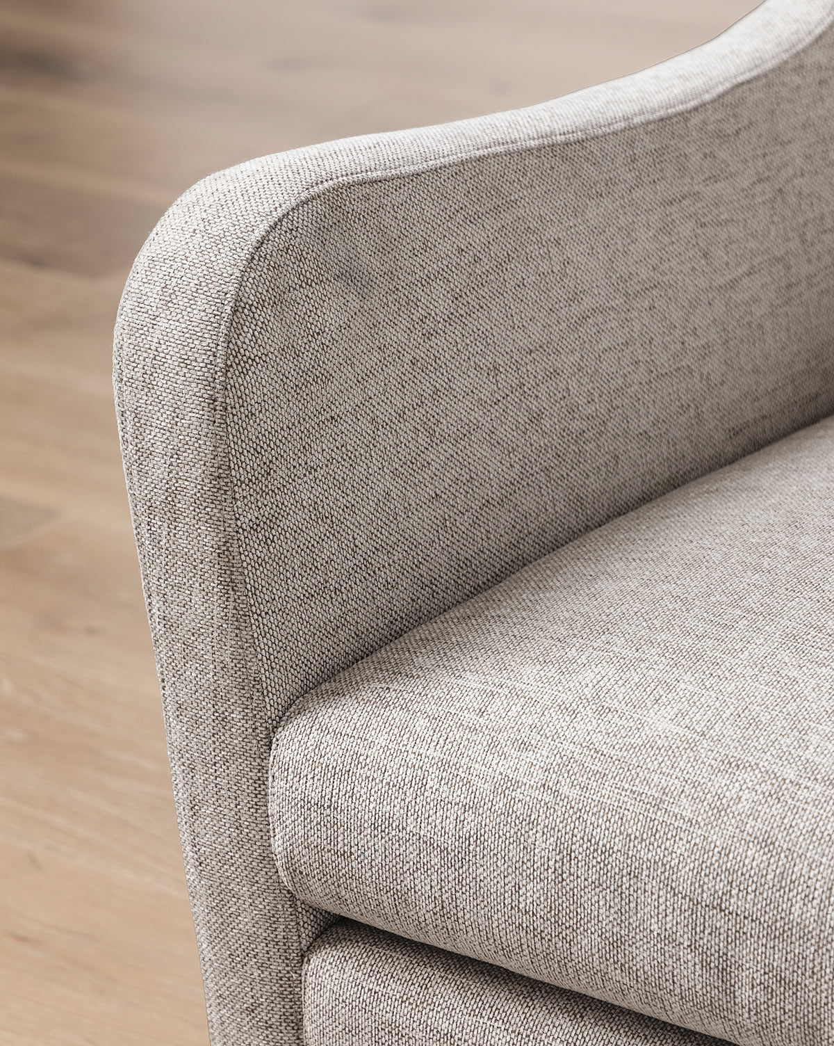 Close-up of the Commodore Lounge Chair, featuring deep seating, light gray twine crypton upholstery, curved padded armrests and seat cushion, placed on a wooden floor, by McGee & Co.