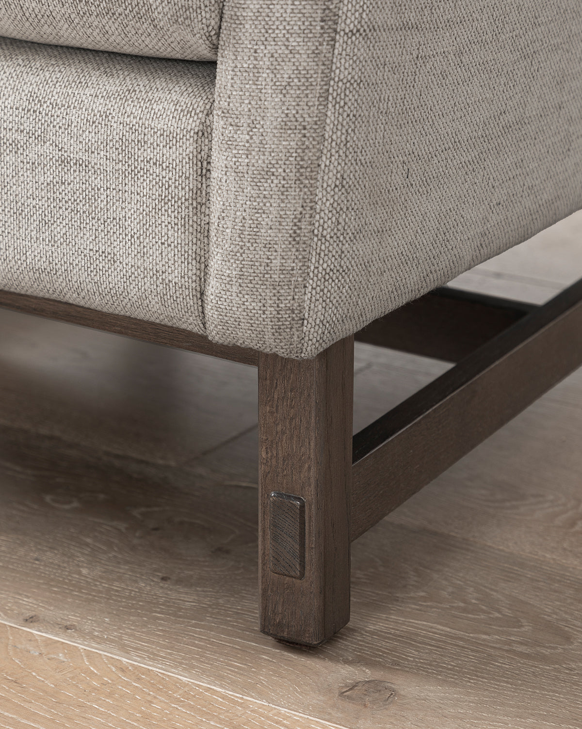 Close-up of the Commodore Lounge Chair, featuring light beige upholstery with a detailed twine crypton texture, and a wooden base and legs, shown on a light wood floor that highlights its corner design, by McGee & Co.