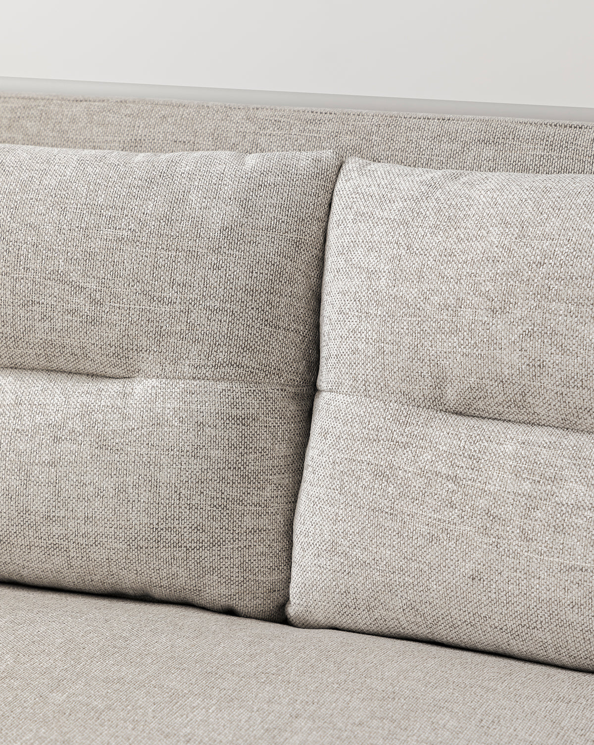 Close-up of the Commodore Settee 68 in modern light gray twine Crypton fabric, featuring two backrest cushions and highlighted texture and stitching details. Set against a plain, light-colored wall by McGee & Co.