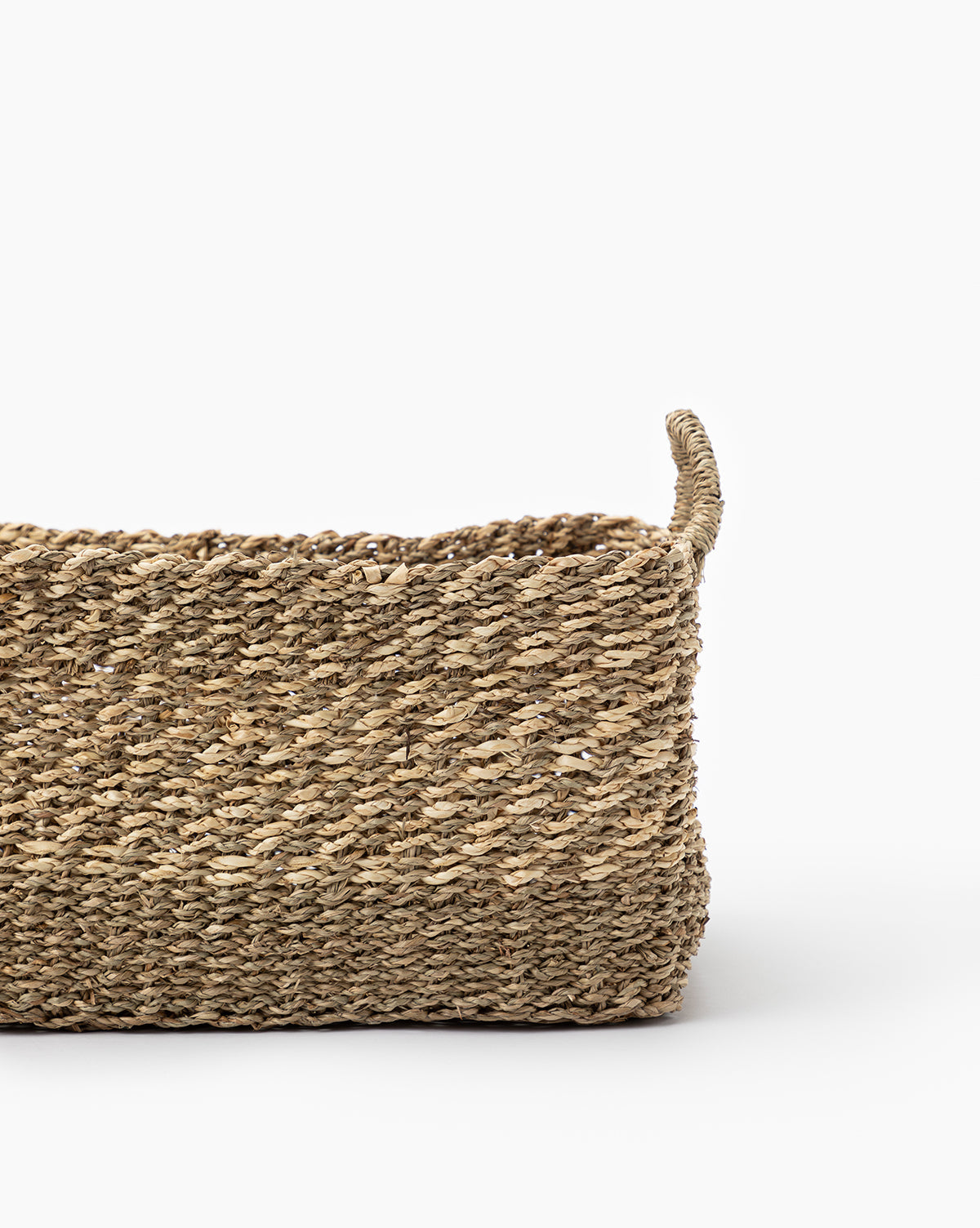 The Cordova Basket, a handled rectangular storage basket crafted from natural fibers, is featured against a plain white background with one handle in view, showcasing its stylish design.