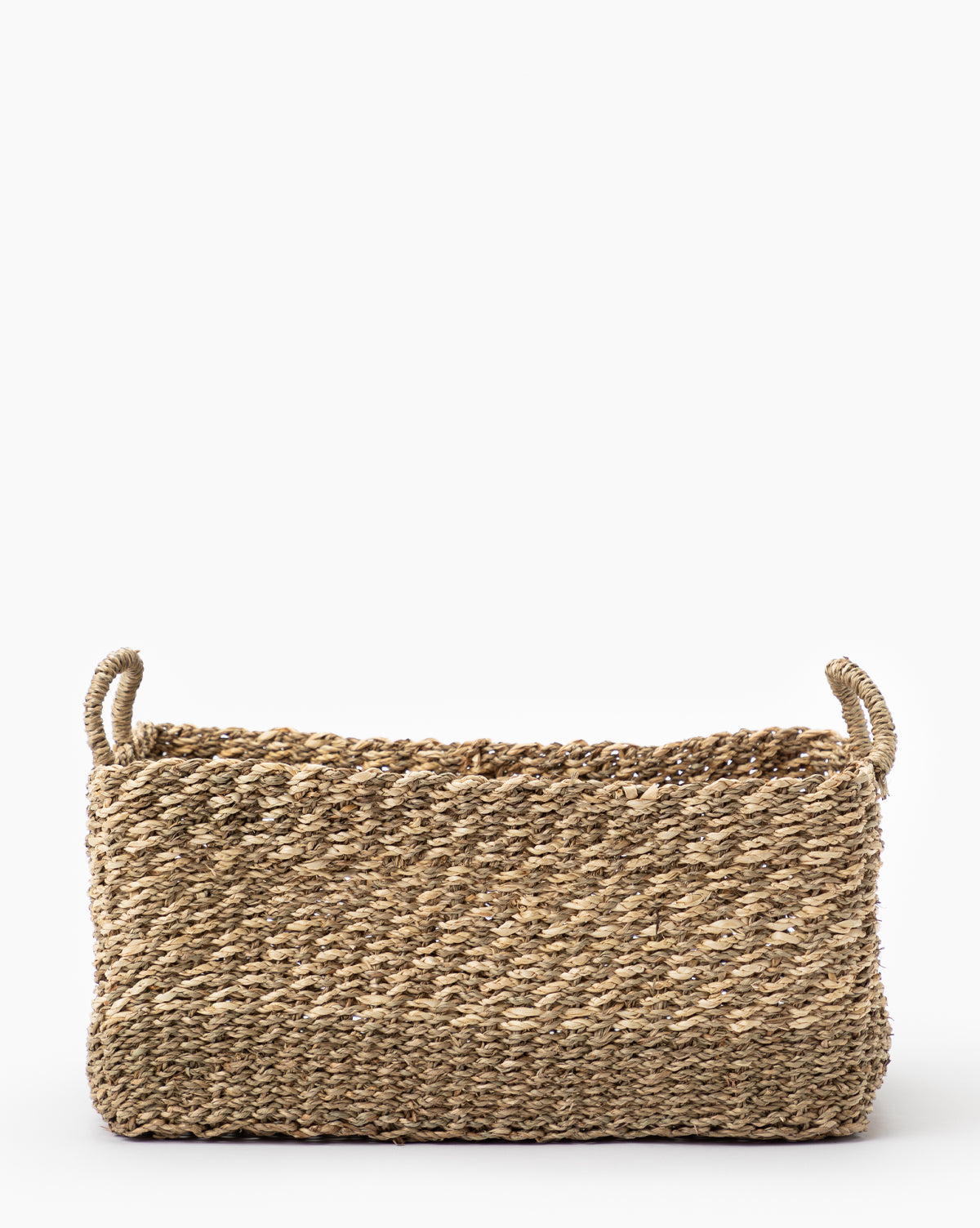 The Cordova Basket is a rectangular woven grass basket with two short side handles, crafted from natural straw or seagrass—ideal for stylish storage. Presented against a plain white background.