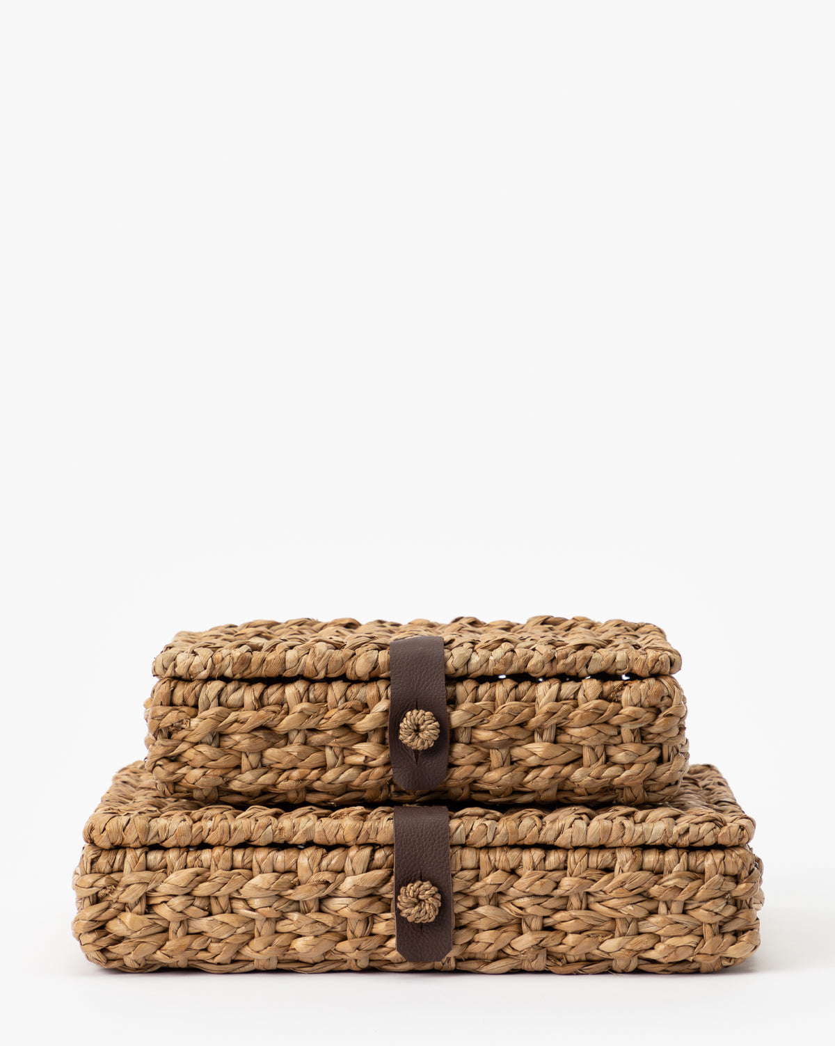 The Corinne Woven Box set features two rectangular seagrass storage baskets with lids and dark brown strap closures, stacked neatly against a white background—perfect for stylish and functional home organization.