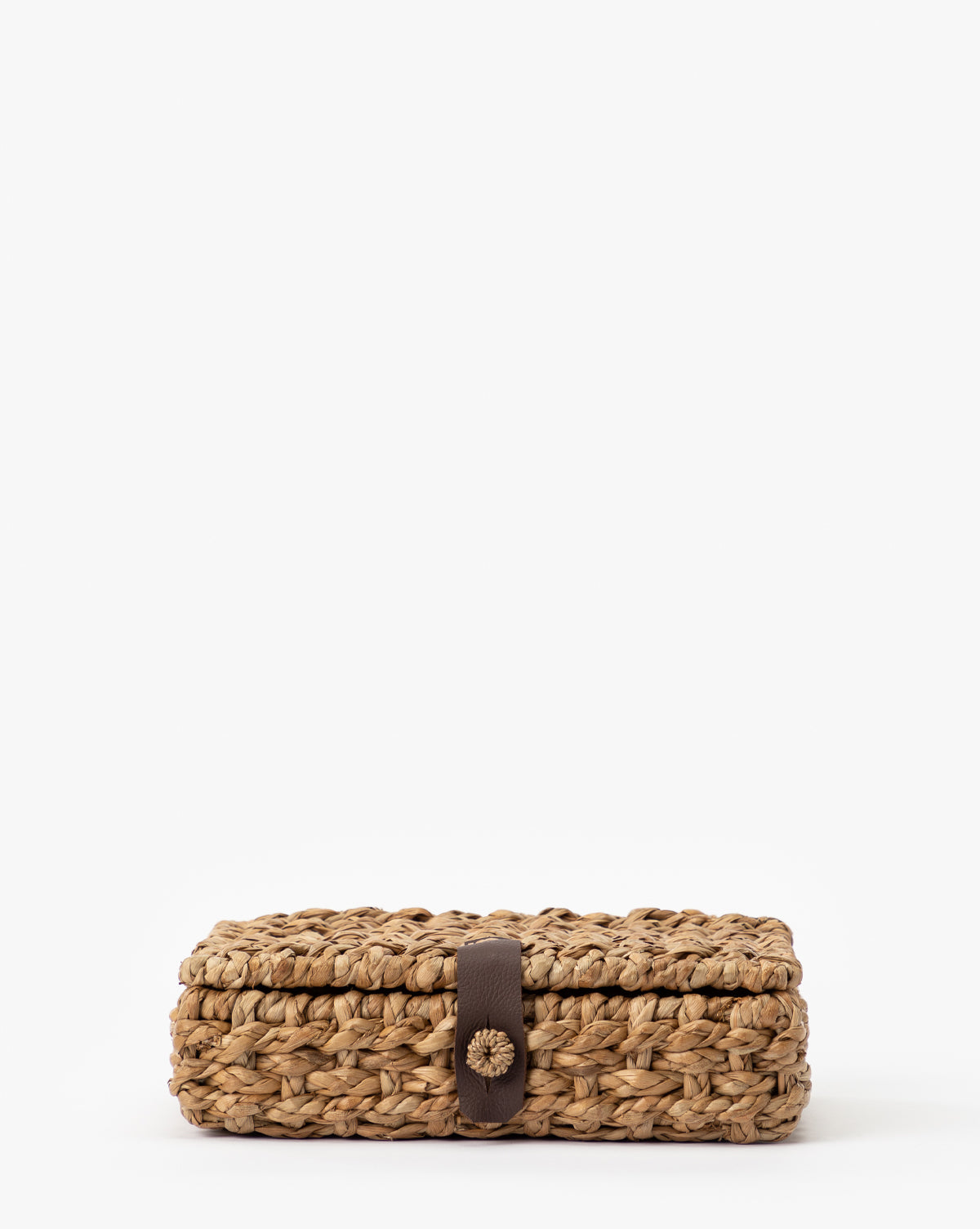 The Corinne Woven Box is a rectangular seagrass box with a lid, brown strap, and button closure, shown on a plain white background.