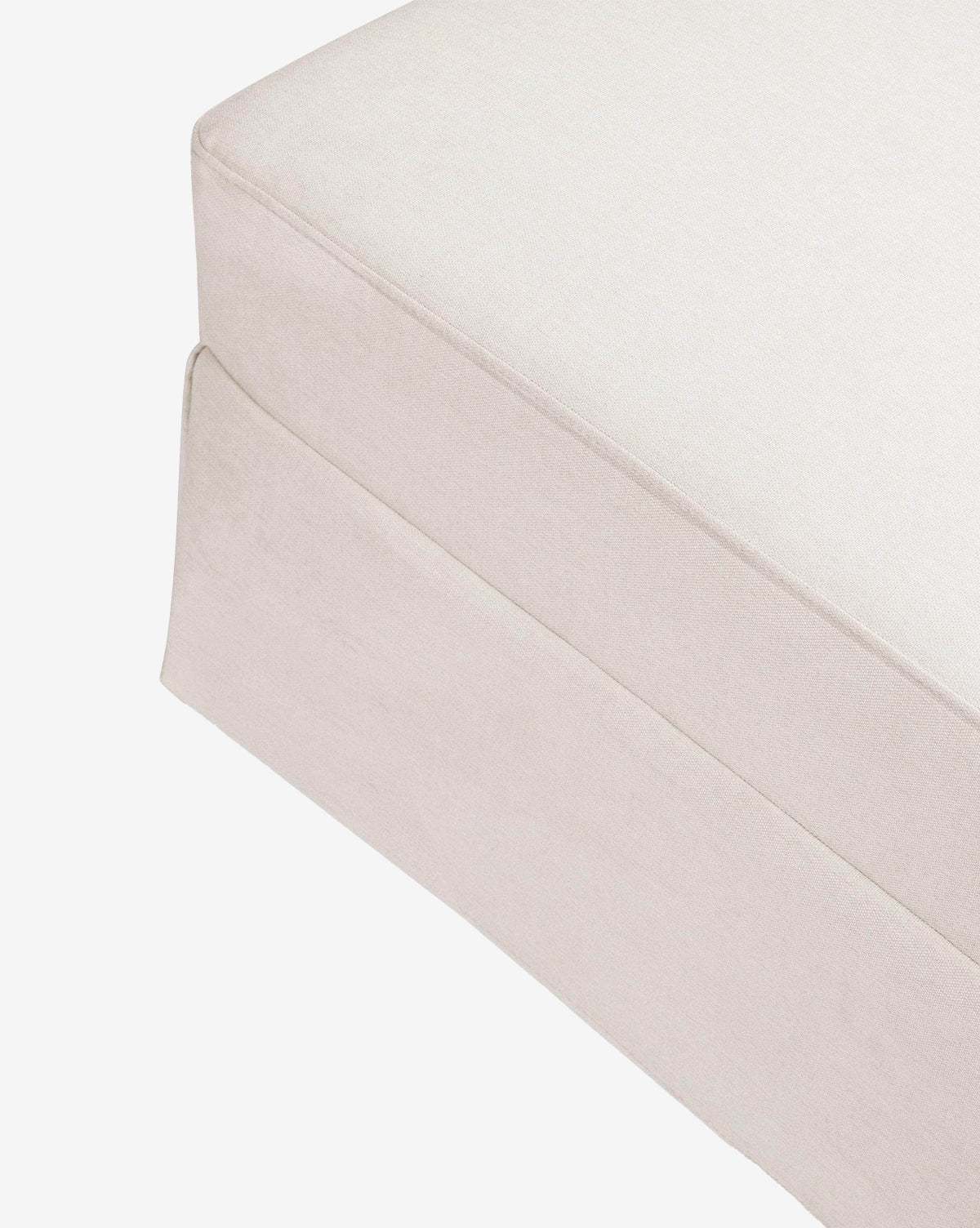 Close-up of the corner of a light beige Million Dollar Baby Crawford Gliding Ottoman with eco-performance upholstery and a tailored skirt, shown on a white background, McGee & Co.