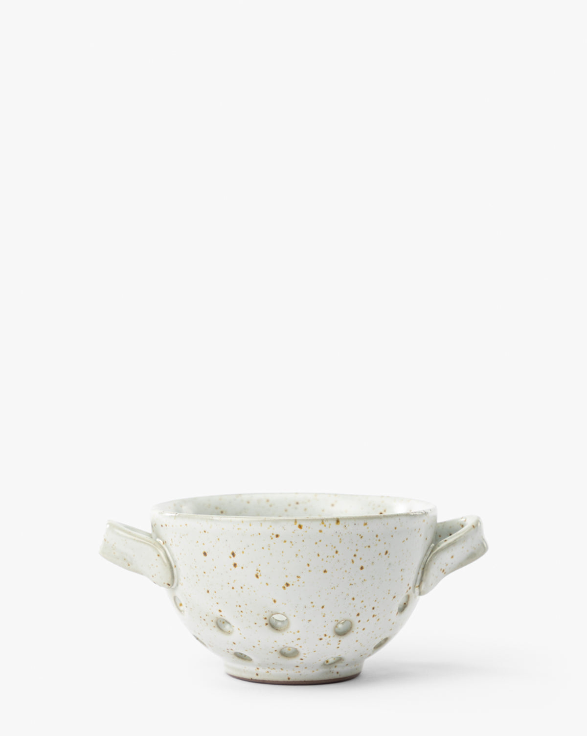 The Cream Handled Berry Bowl is an artisanal, white speckled stoneware bowl featuring two small side handles and several circular perforations, shown on a plain white background by McGee & Co.