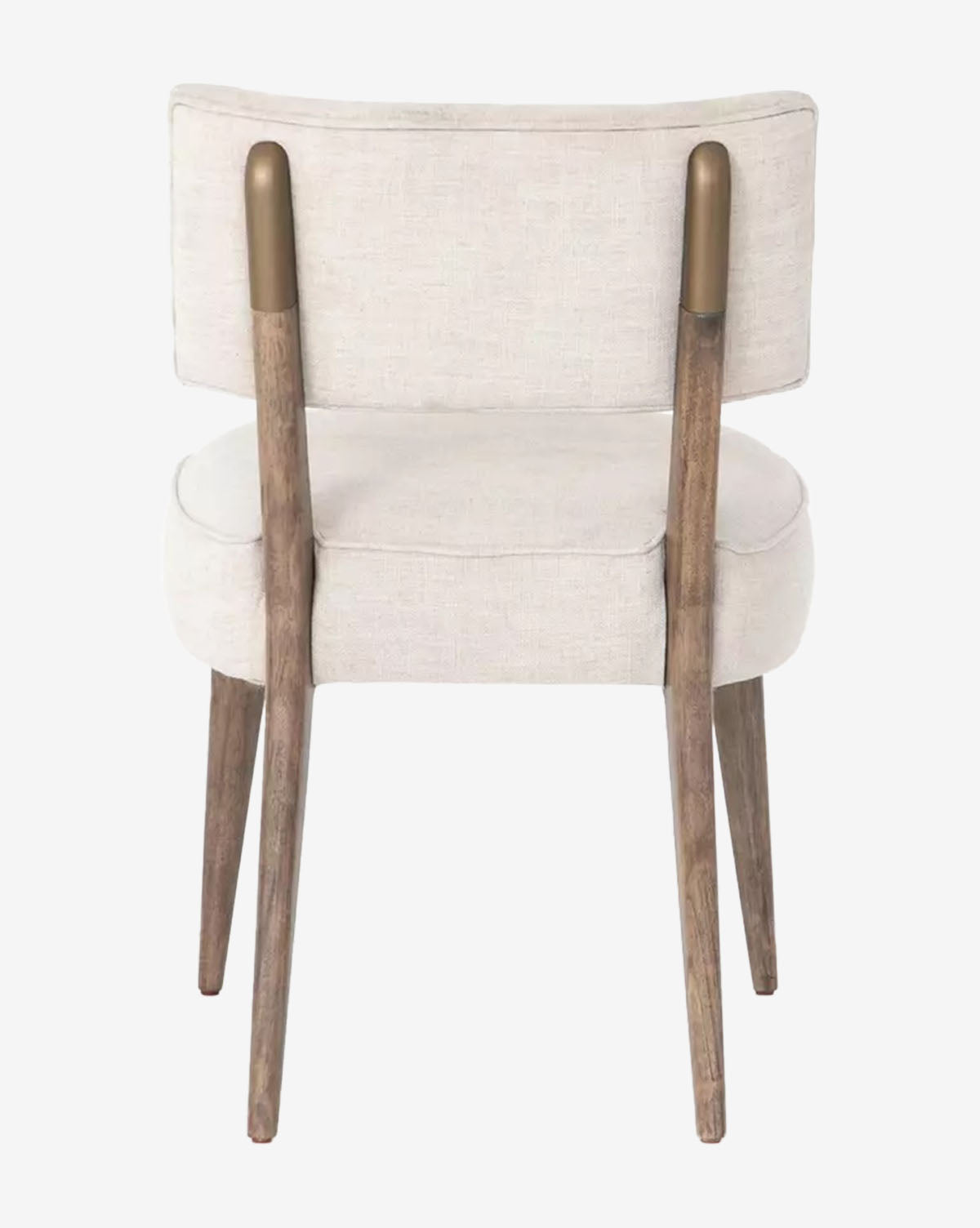 The Cyrene Dining Chair showcases a modern design with an ivory performance fabric seat and back, four angled wood legs, and two wooden back supports with gold-toned caps, by McGee & Co. The image displays the chair from the back.