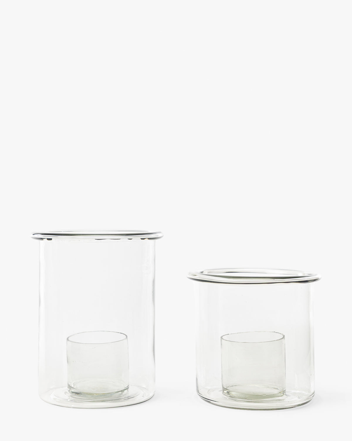 The Cyrus Hurricane set features two clear glass candle holders of varying heights, each with an inner cylindrical glass, shown side by side on a white background—ideal for elegant home decor, by McGee & Co.