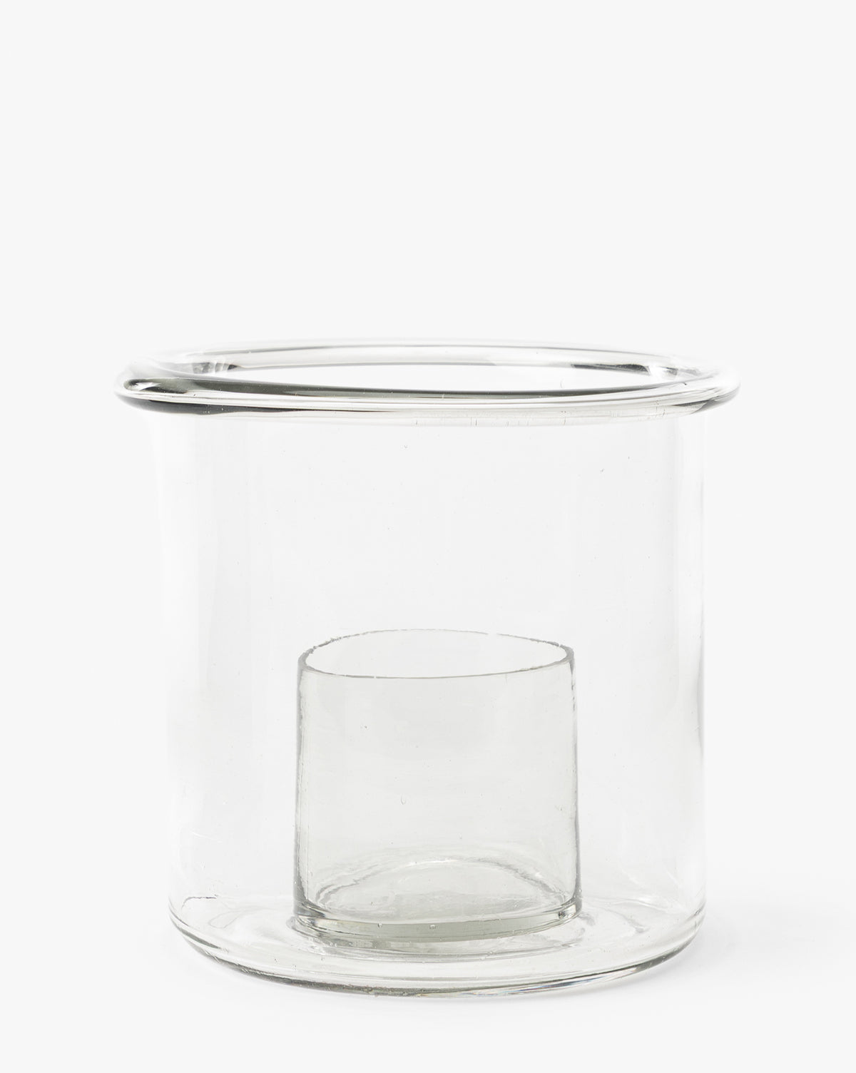 The Cyrus Hurricane is a clear glass candle holder with thick walls, a cylindrical shape, and an inner compartment at the base. Featuring a smooth wide rim, its perfect for stylish home decor by McGee & Co.