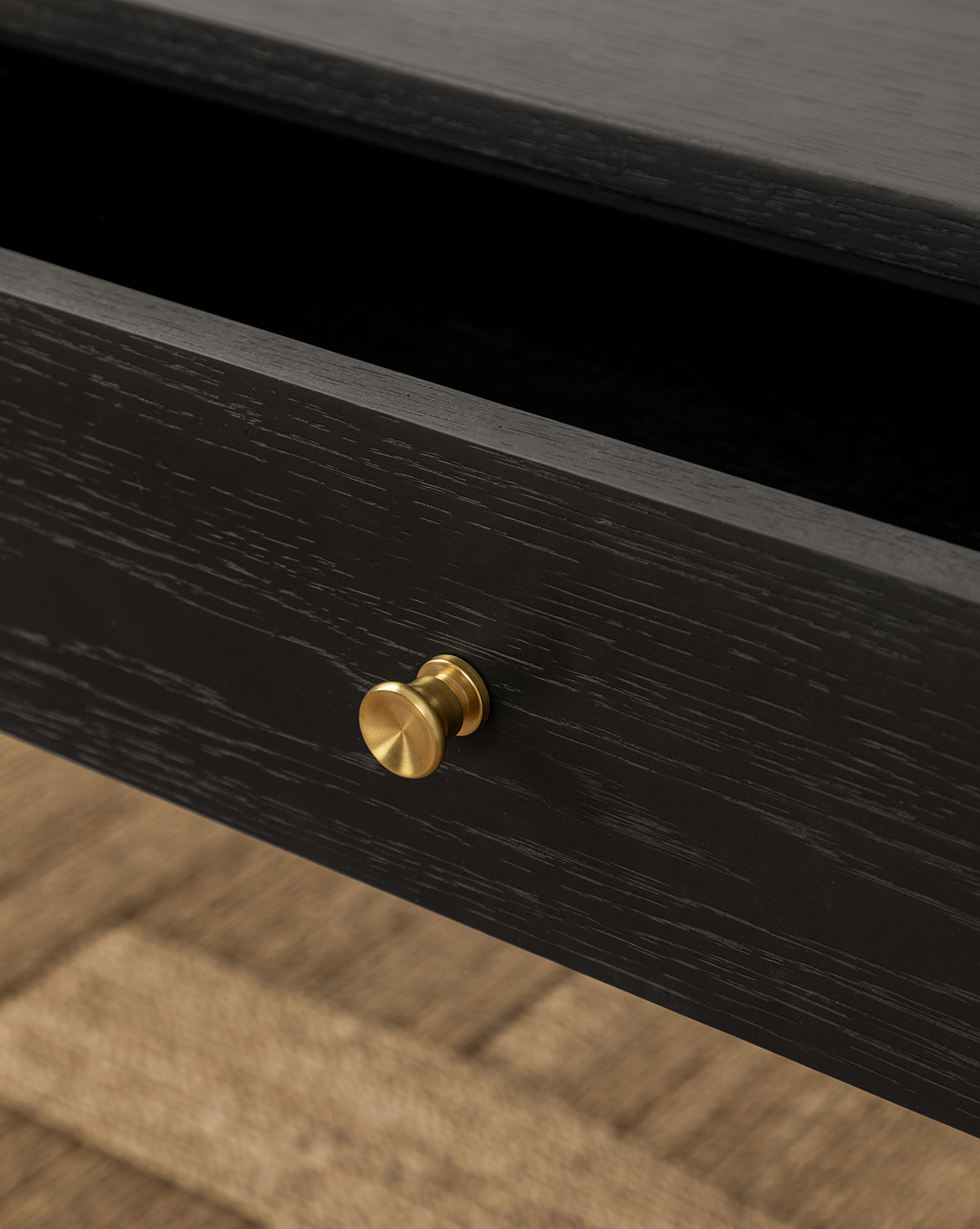 A close-up of an open black wooden drawer with a round gold knob from the Dana 2-Drawer Console, set on a textured light brown floor—ideal for adding style to your entryway, by McGee & Co.