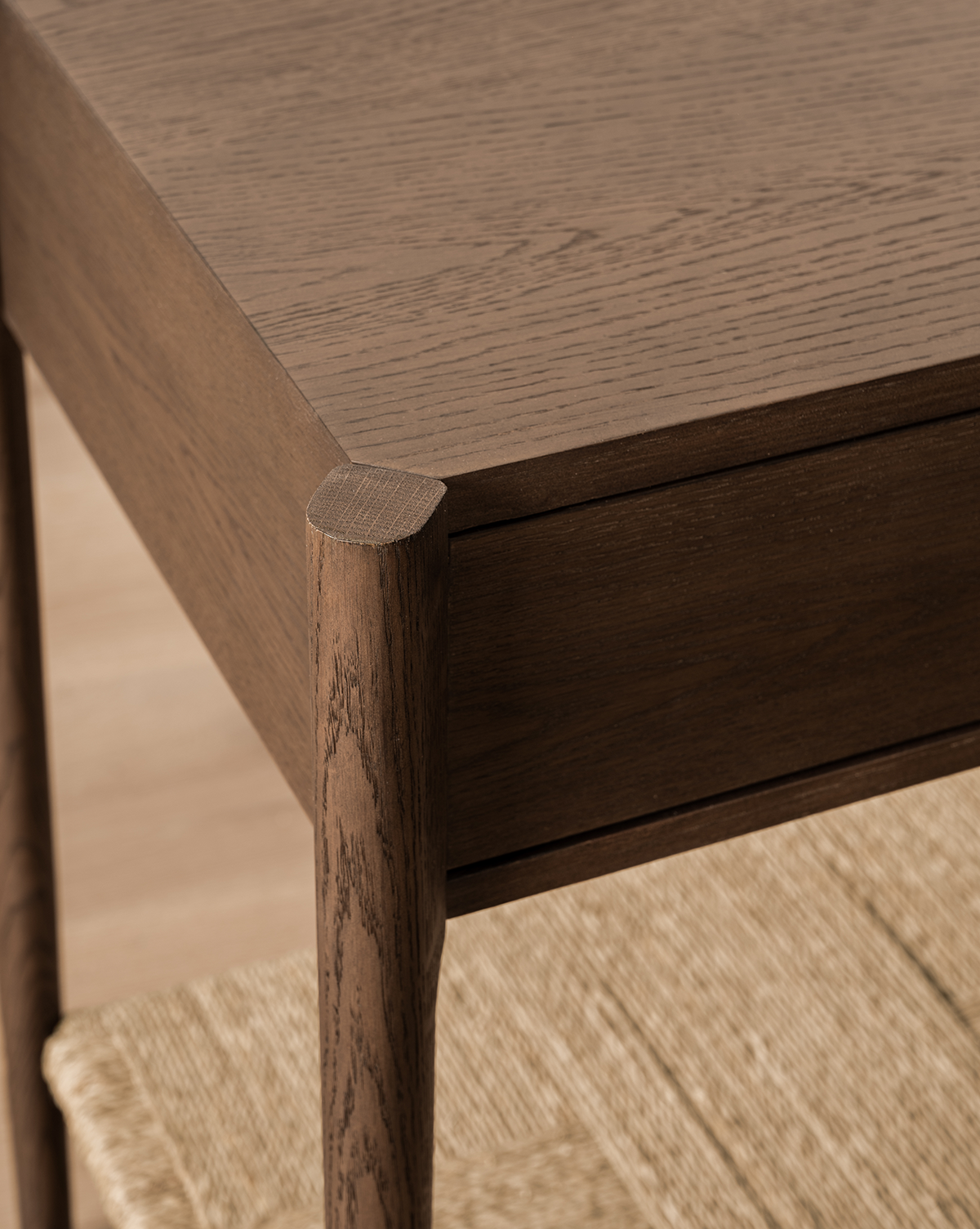 Close-up of the Dana Walnut Oak Console’s corner, featuring rounded legs, a smooth dark finish, and a partially visible woven shelf beneath, by McGee & Co.