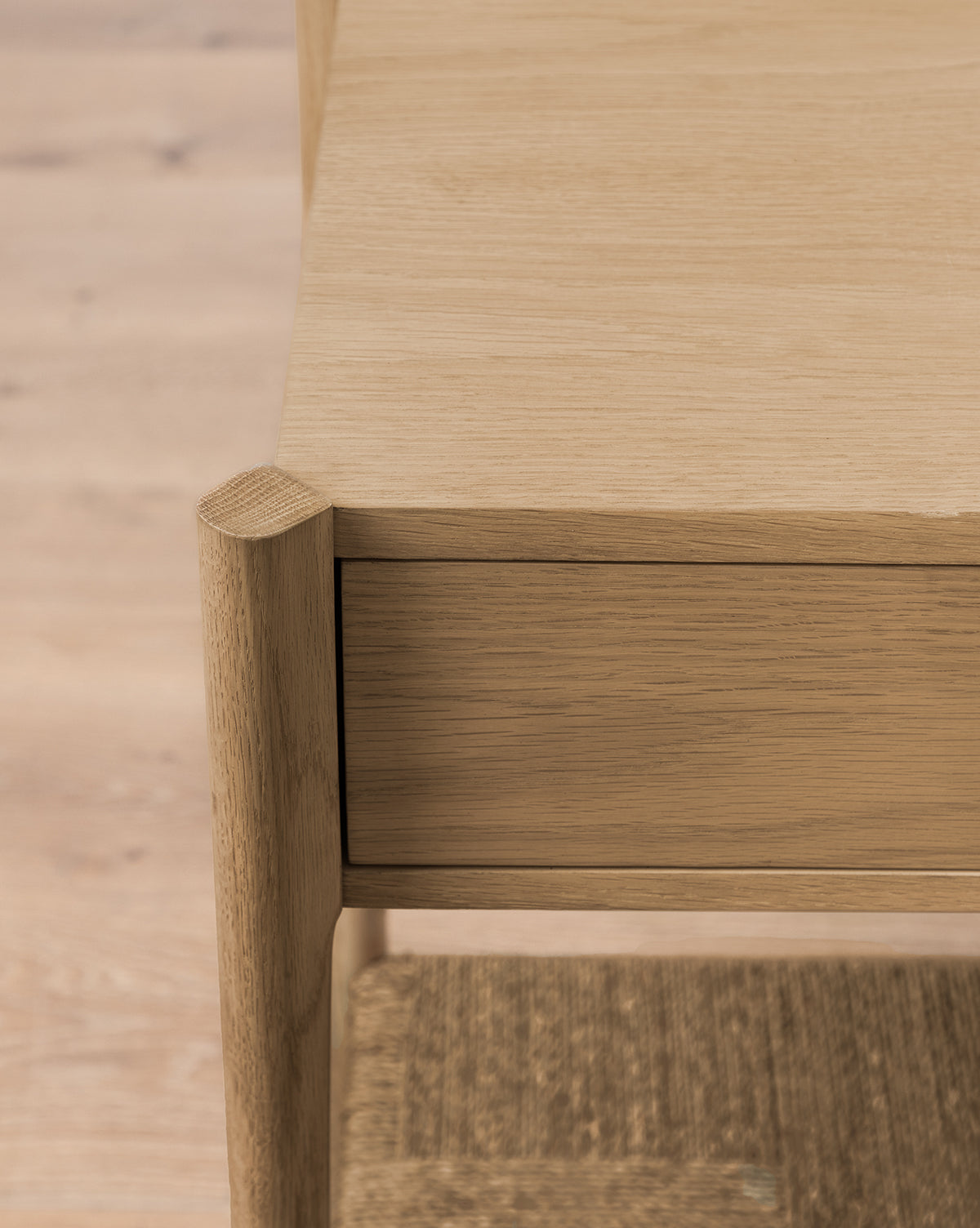 Close-up of the Dana White Oak Console’s corner, featuring soft close drawers with a natural light wood grain finish. The lower shelf is crafted from woven seagrass for added texture and style, by McGee & Co.