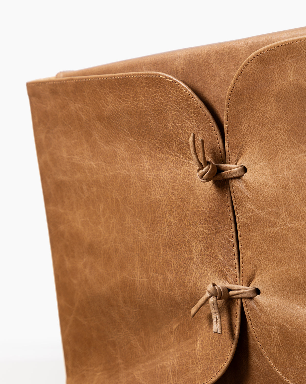 Close-up of the Danson Dining Chair with a light brown leather seat featuring a textured surface and minimalist design. Two leather straps tied in knots secure the flap, while a plain white background highlights its expert craftsmanship, by McGee & Co.