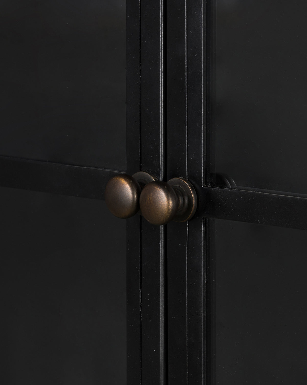 Close-up of two round bronze knobs on the Darcie Wide Cabinet’s iron frame doors. The cabinet features dark metal-framed glass doors with intersecting frames and side-by-side knobs, by McGee & Co.