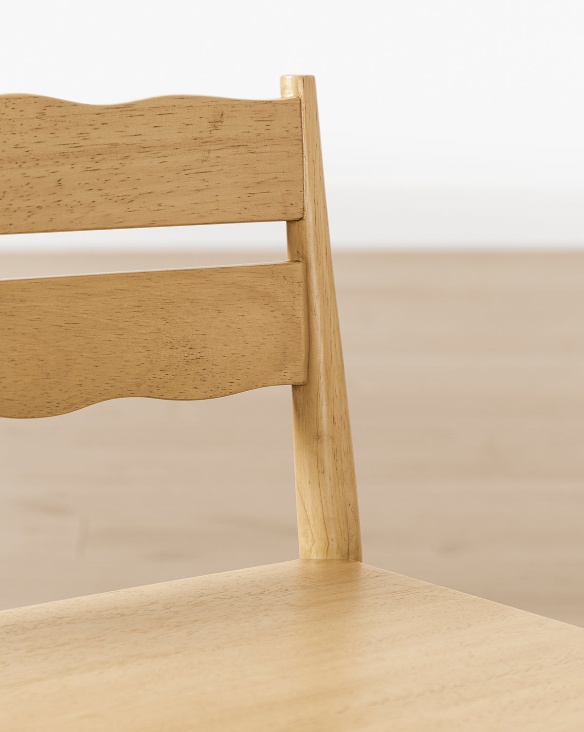 Close-up of a Darcy Kids Chair from the Darcy Kids Chairs (Set of 2), featuring a light wood finish, backrest with two horizontal slats—one with a wavy edge—and a softly blurred background that highlights this stylish play chair, by McGee & Co.