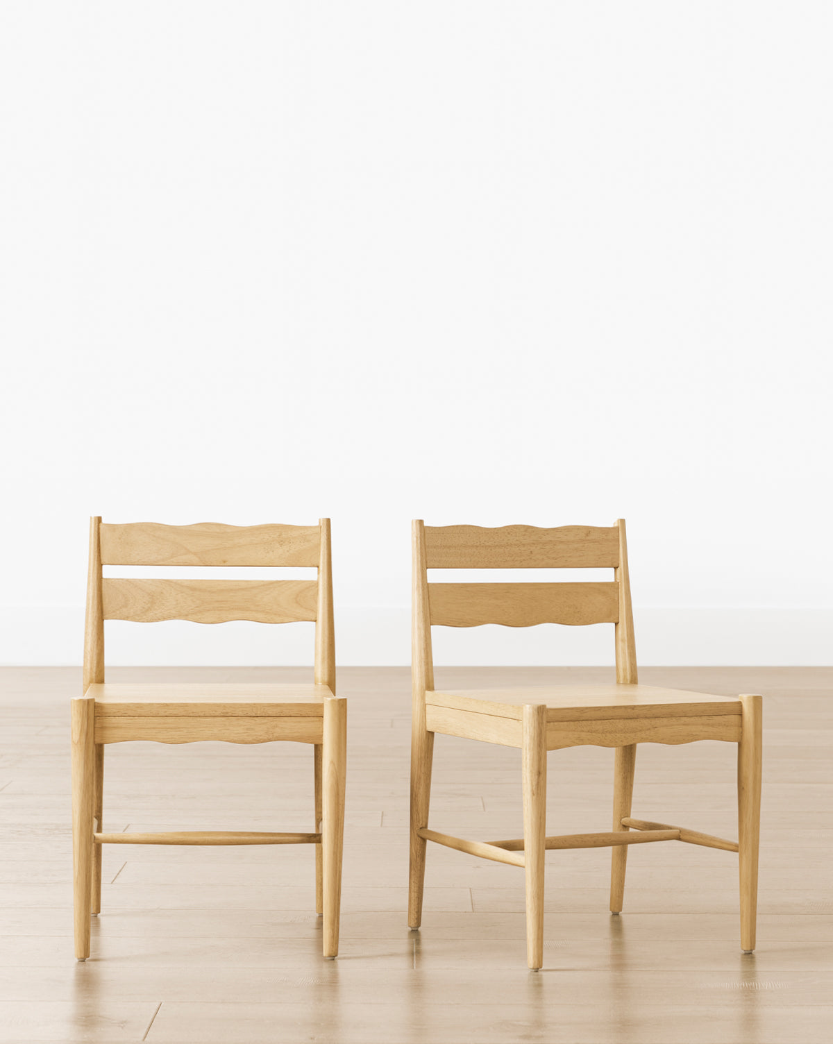 Two Darcy Kids Chairs (Set of 2), made from light-colored wood with wavy slatted backrests, stand on a light wood floor against a plain white wall—stylish and sturdy seating for any kids’ play area, by McGee & Co.