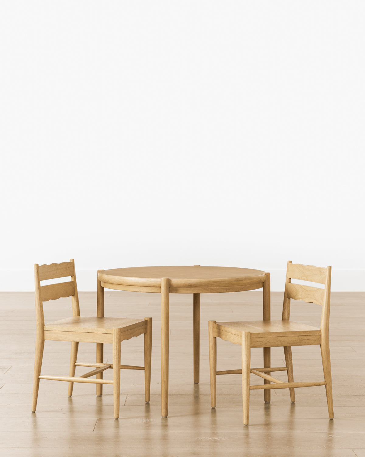 The Darcy Kids Table is arranged with two simple white oak chairs on a light wood floor against a plain white background, by McGee & Co.