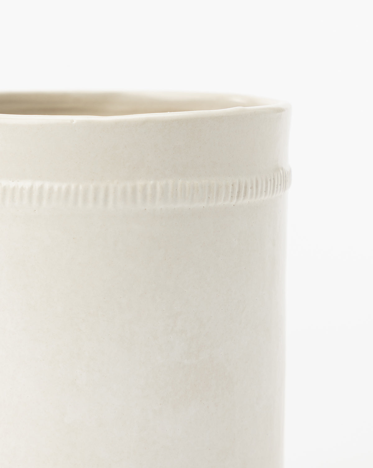A close-up of the Dashed Ceramic Crock displays its smooth off-white ceramic finish with a subtle horizontal line and vertical indentations near the rim, making it elegant decor for any kitchen countertop against a plain white background.