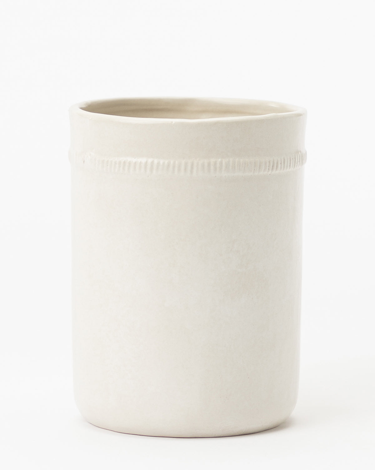 The Dashed Ceramic Crock is a simple, cylindrical off-white ceramic cup with a smooth matte finish and a subtle ridge near the rim, evoking minimalist vase design, displayed against a plain white background.
