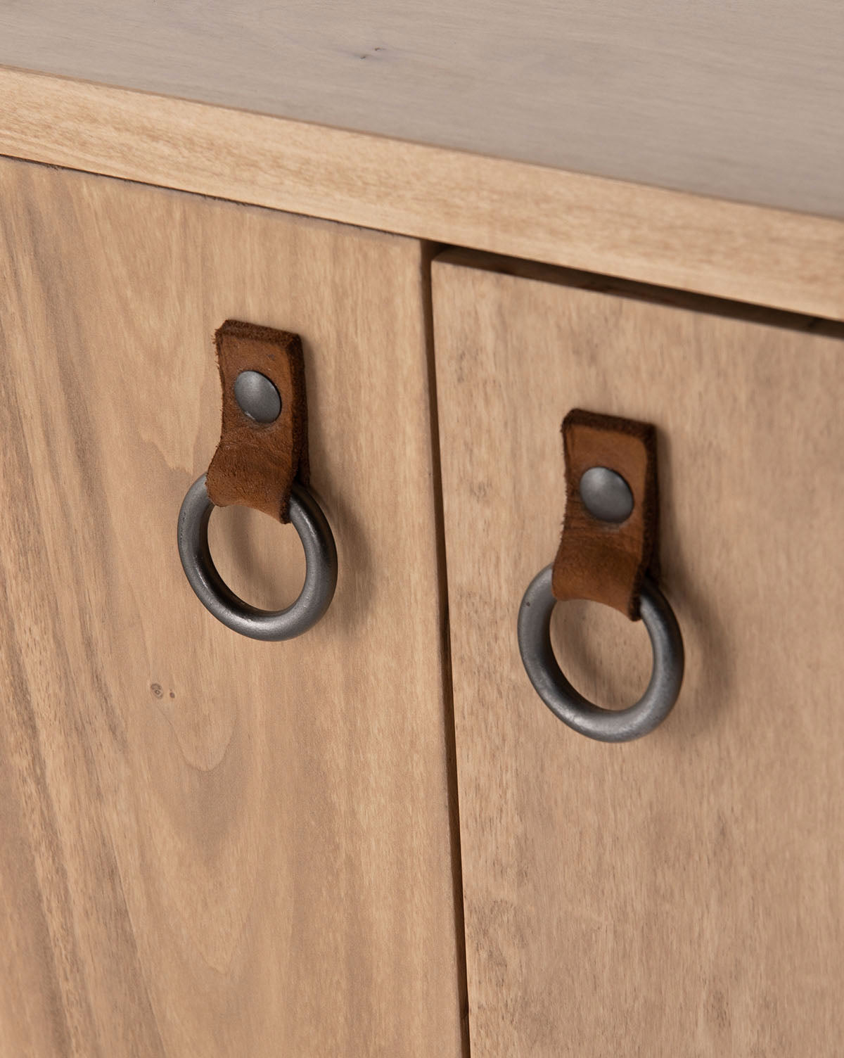 Close-up of two shaker-inspired wooden cabinet doors on the Daylin Sideboard, featuring round metal ring handles with brown leather straps and metal rivets. The light wood finish highlights a subtle grain pattern, by McGee & Co.