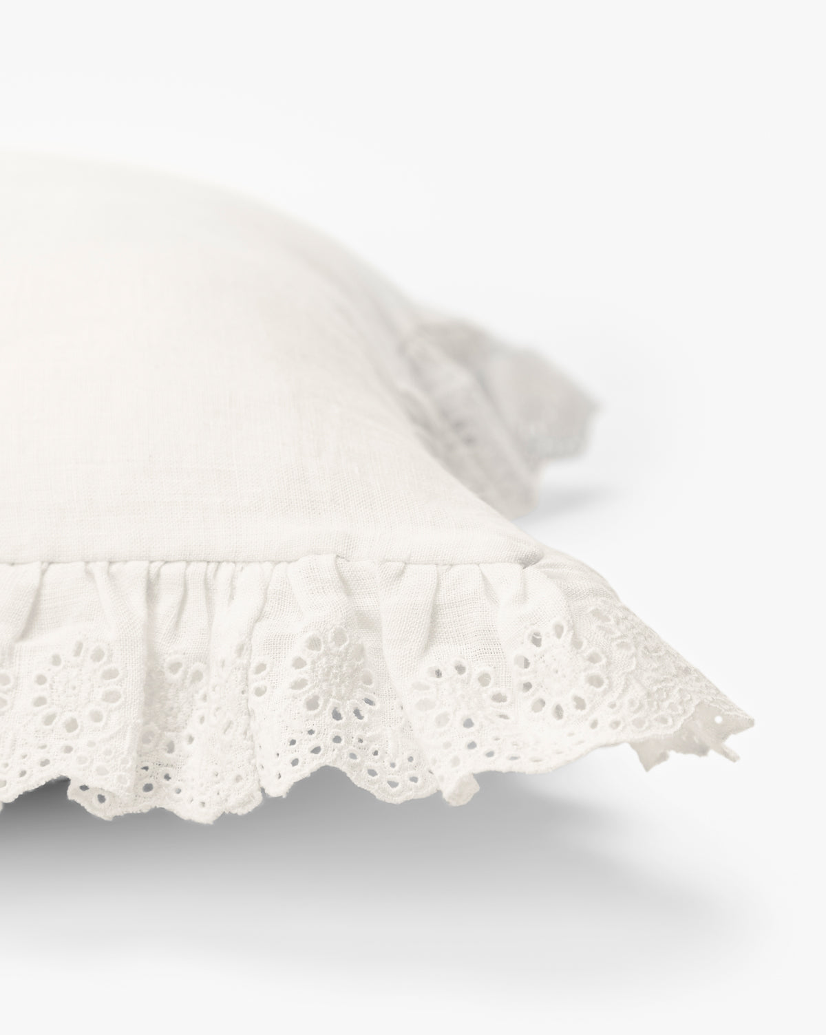 A close-up of the McGee & Co. x Loeffler Randall Delilah Broderie Trim Pillow Cover shows its white linen, ruffled lace edges, and delicate cut-out embroidery, with a light background that highlights its soft texture and intricate detailing by McGee & Co.