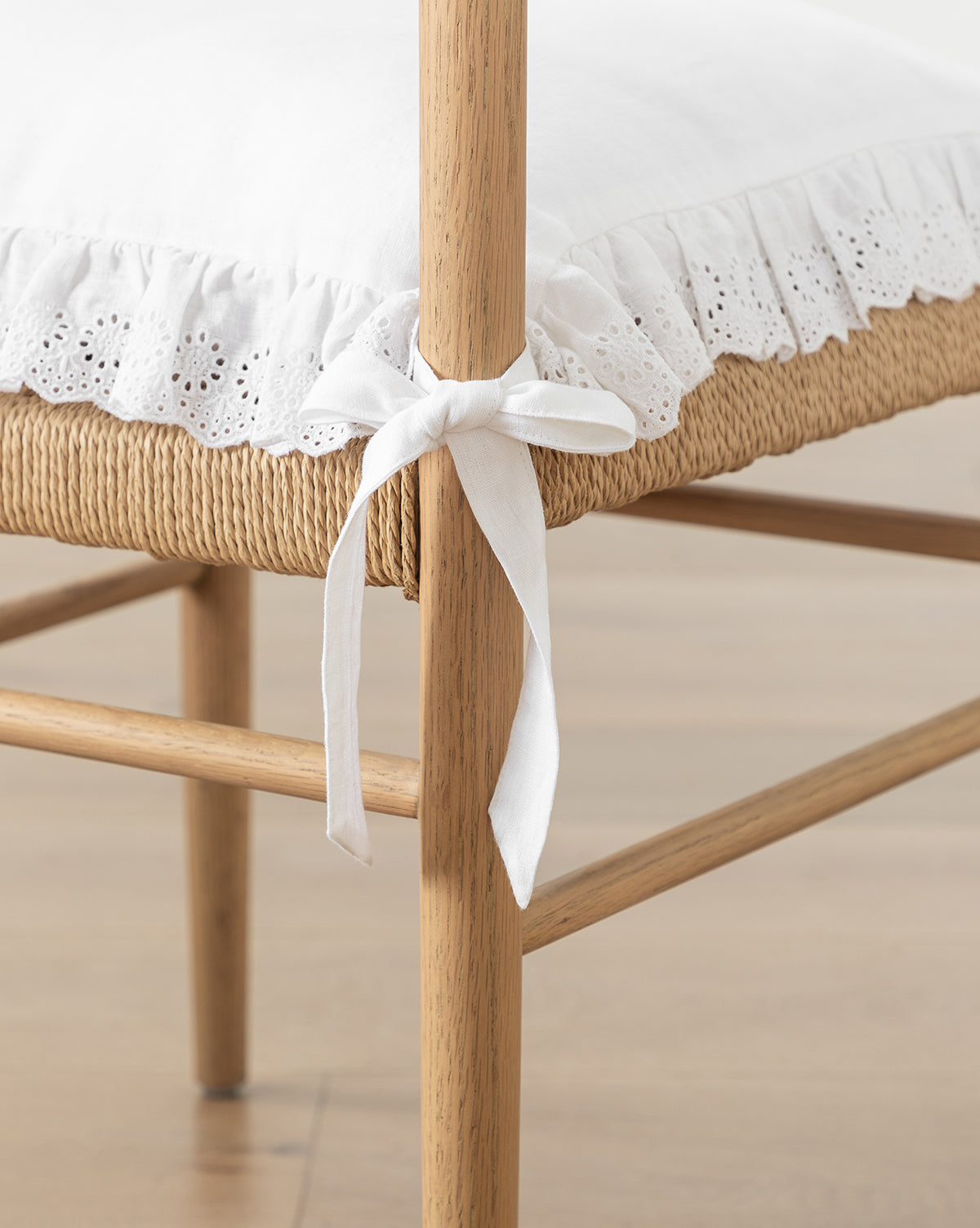 Sure! Here’s your blended sentence with the exact string McGee & Co. at the end: Close-up of a wooden chair with a woven seat, featuring the McGee & Co. x Loeffler Randall Delilah Broderie Trim Seat Cushion, secured with a fabric tie bow, McGee & Co.