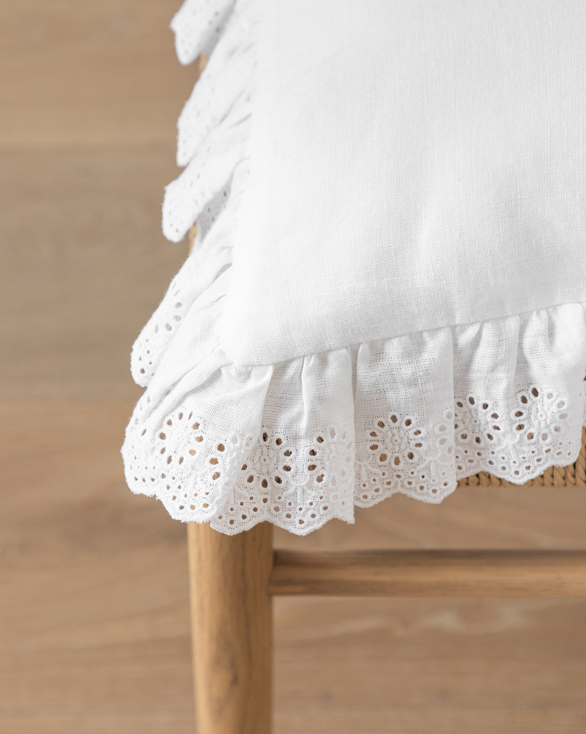 Certainly! Here’s your sentence with the exact string McGee & Co. blended at the end: The McGee & Co. x Loeffler Randall Delilah Broderie Trim Seat Cushion, featuring white linen and eyelet lace ruffles, rests on a wooden chair with a woven seat, adding delicate texture above the light wood floor by McGee & Co.