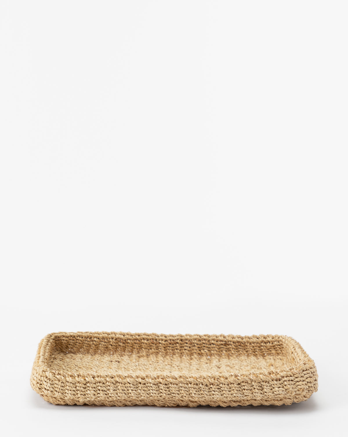 The Deryn Woven Tray is a rectangular coffee table tray made from abaca fibers with raised edges, displayed elegantly on a white background.