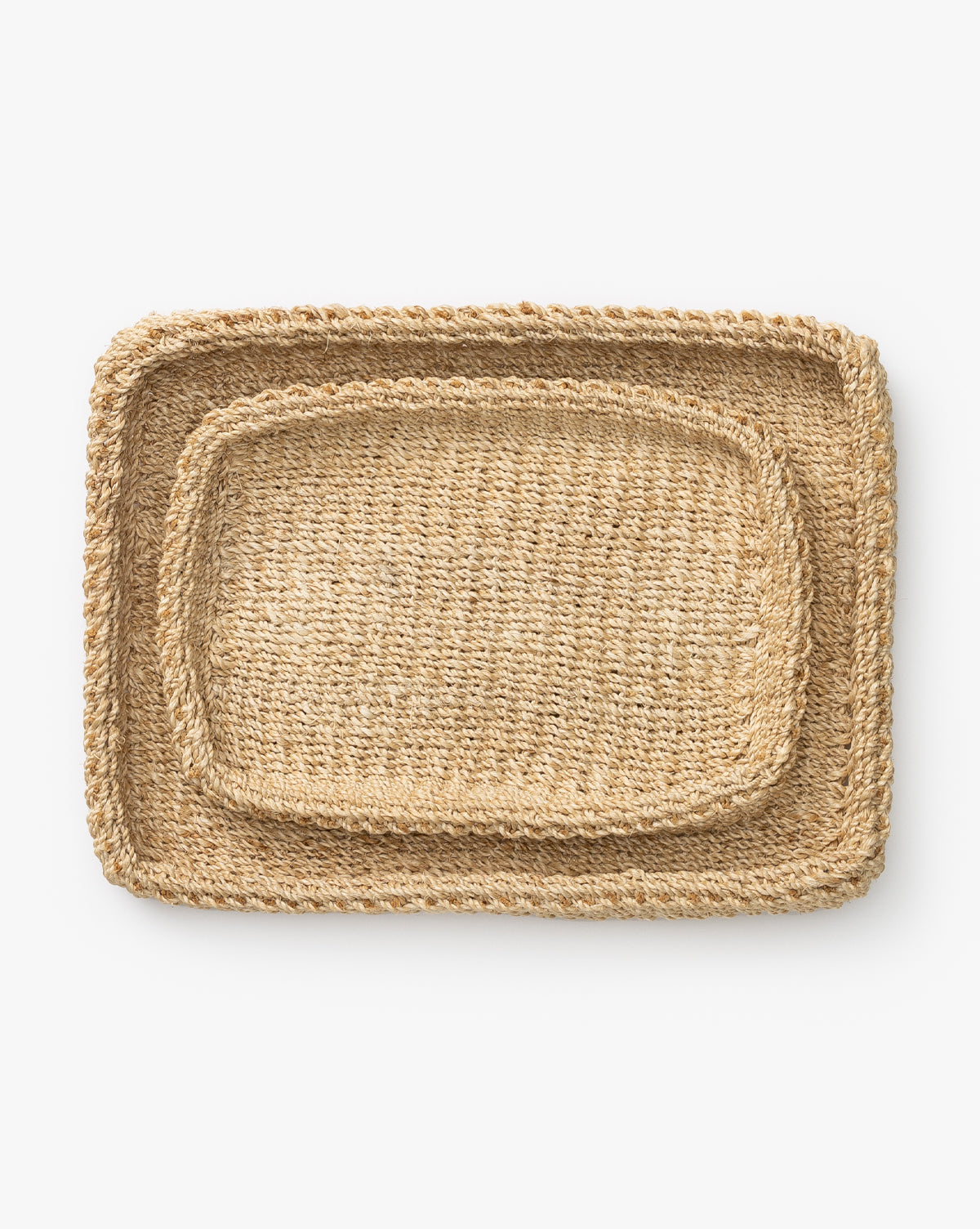 Two Deryn Woven Trays made of natural abaca fiber, featuring braided edges—one smaller coffee table tray nested inside a larger tray—are displayed on a white background.