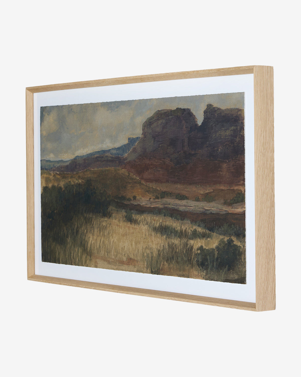 Desert Hues I by Aileen Fitzgerald is a framed landscape print on fine art paper, depicting grassy fields and rocky hills under a cloudy sky. Set in white oak, it features soft, muted earth tones for a serene look, by McGee & Co.