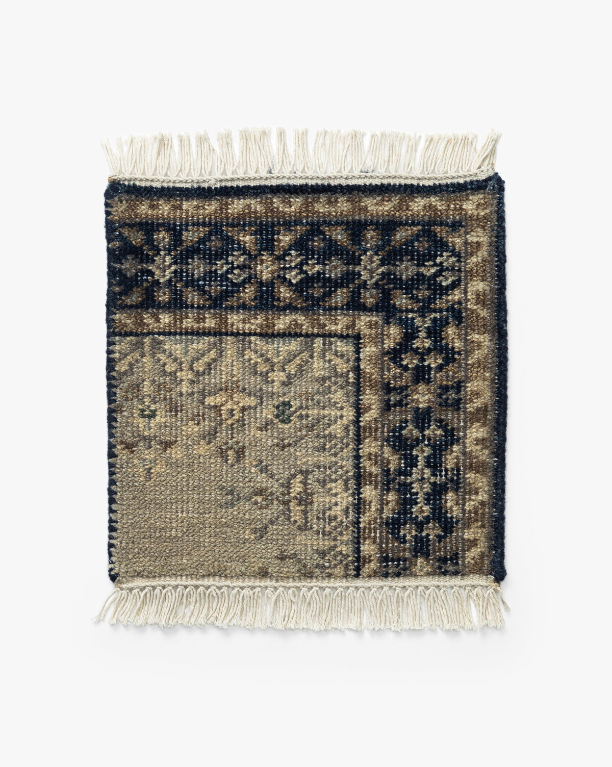 The Deveraux Hand-Knotted Wool Rug Swatch is a square, vintage-inspired sample with cream fringe and a traditional floral pattern in navy, beige, and brown. Part of the wool swatch is folded to show its reverse side, by McGee & Co.