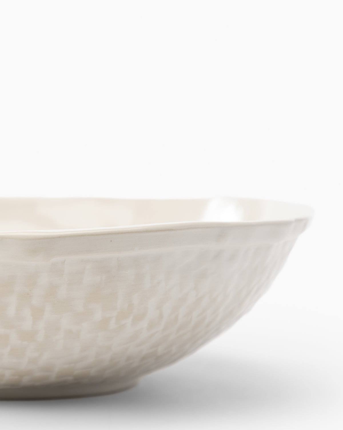 A close-up of the Dion Serving Bowl, a cream-colored ceramic piece with a woven basket design and slightly irregular rim, set against a plain white background, by McGee & Co.