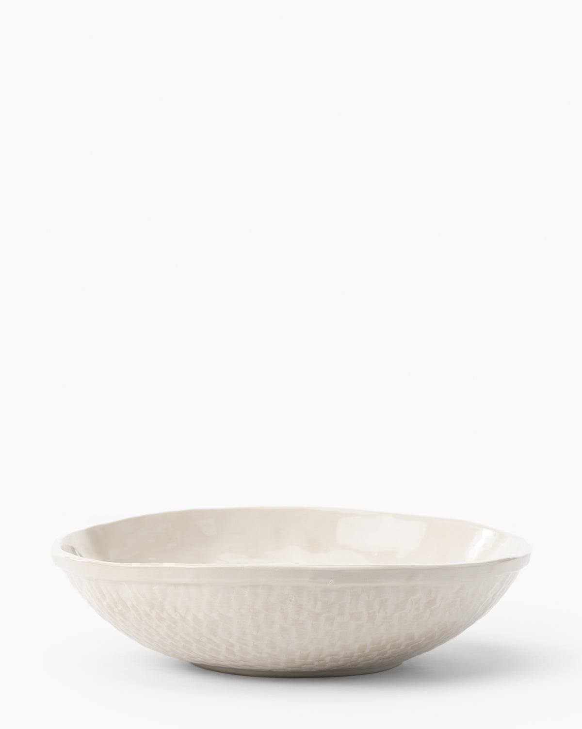 The Dion Serving Bowl is a shallow, round ceramic bowl with a subtle woven basket design on the exterior and an off-white glaze, displayed against a plain white background, by McGee & Co.