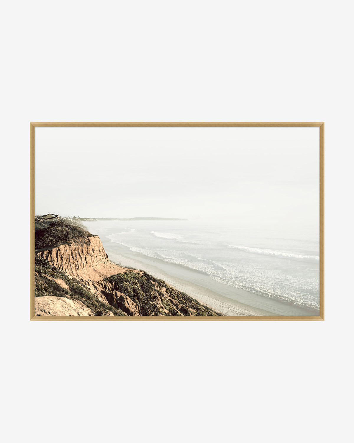 A framed art photograph titled Distant Coastline, featuring sandy cliffs to the left and gentle waves on a broad beach beneath a pale, hazy sky.