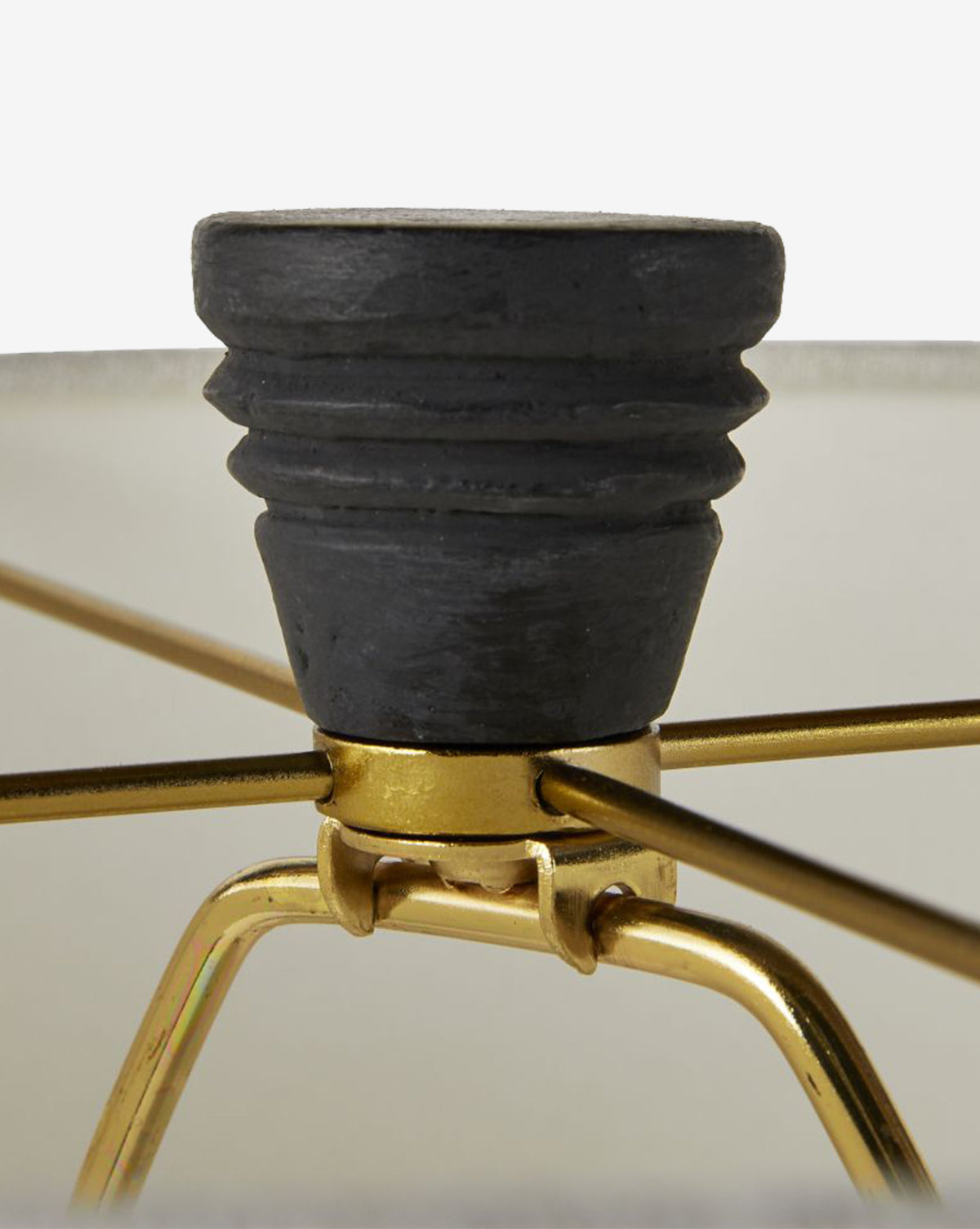 Close-up of the Django Table Lamp’s black, ridged finial atop its linen shade, with visible gold metal frame supports. The background is blurred, by McGee & Co.