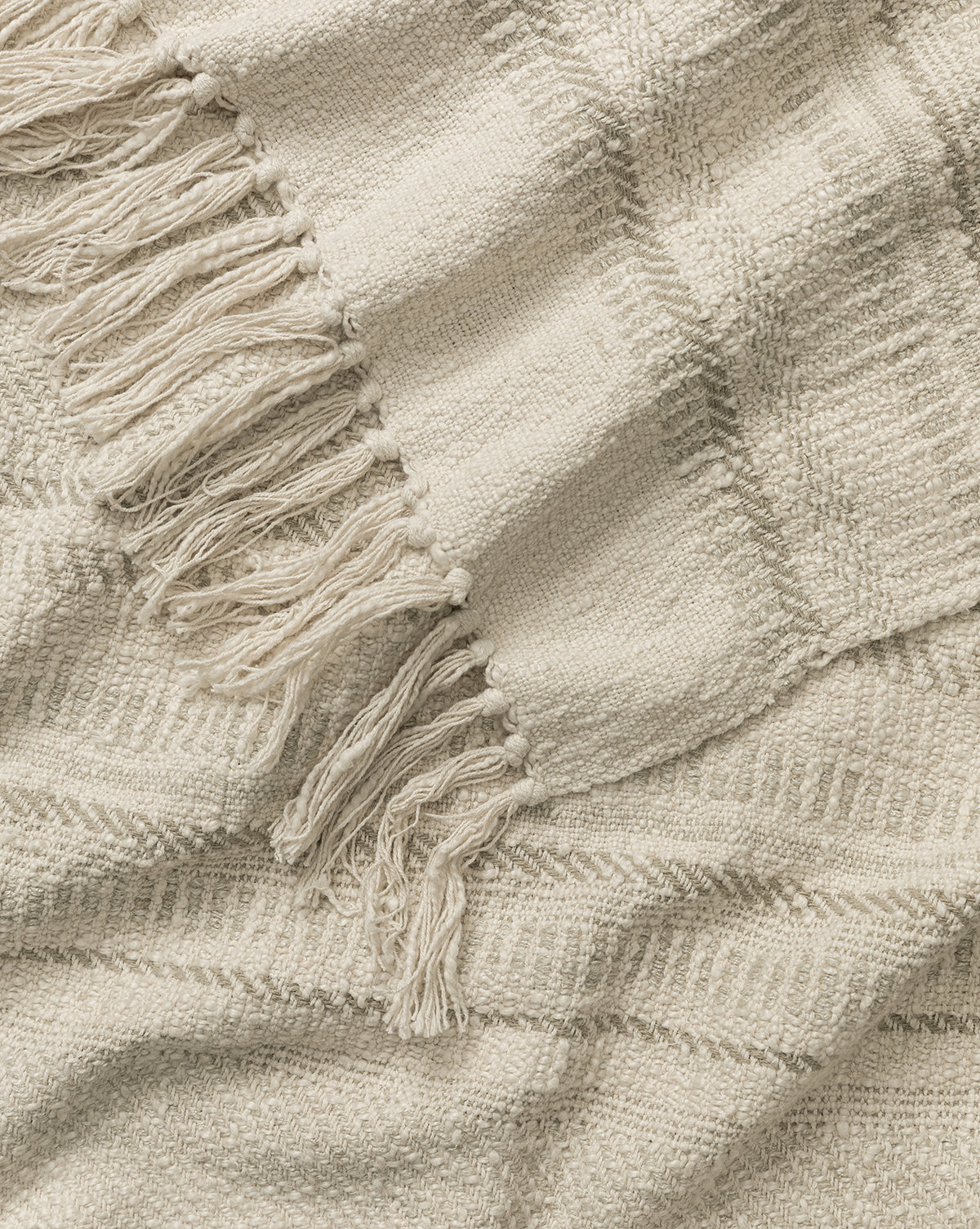 A close-up of the Donahue Striped Throw by ILA HOME FASHIONS, a cream cotton-blend blanket with fringed edges and subtle stripes. This soft, cozy throw adds warmth and texture to any space—Studio McGee & Co.