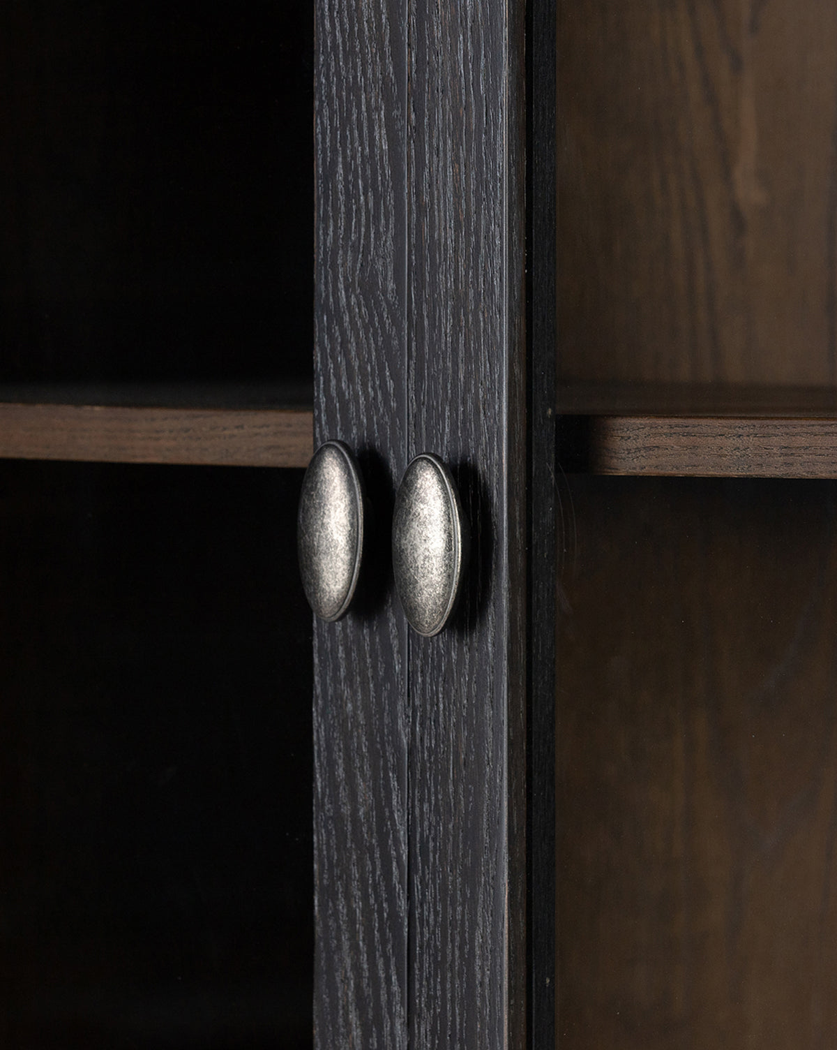 Close-up of the Draven Cabinet’s distressed black doors with oval metallic handles, showcasing the wood grain and a peek at the interior shelf by McGee & Co.