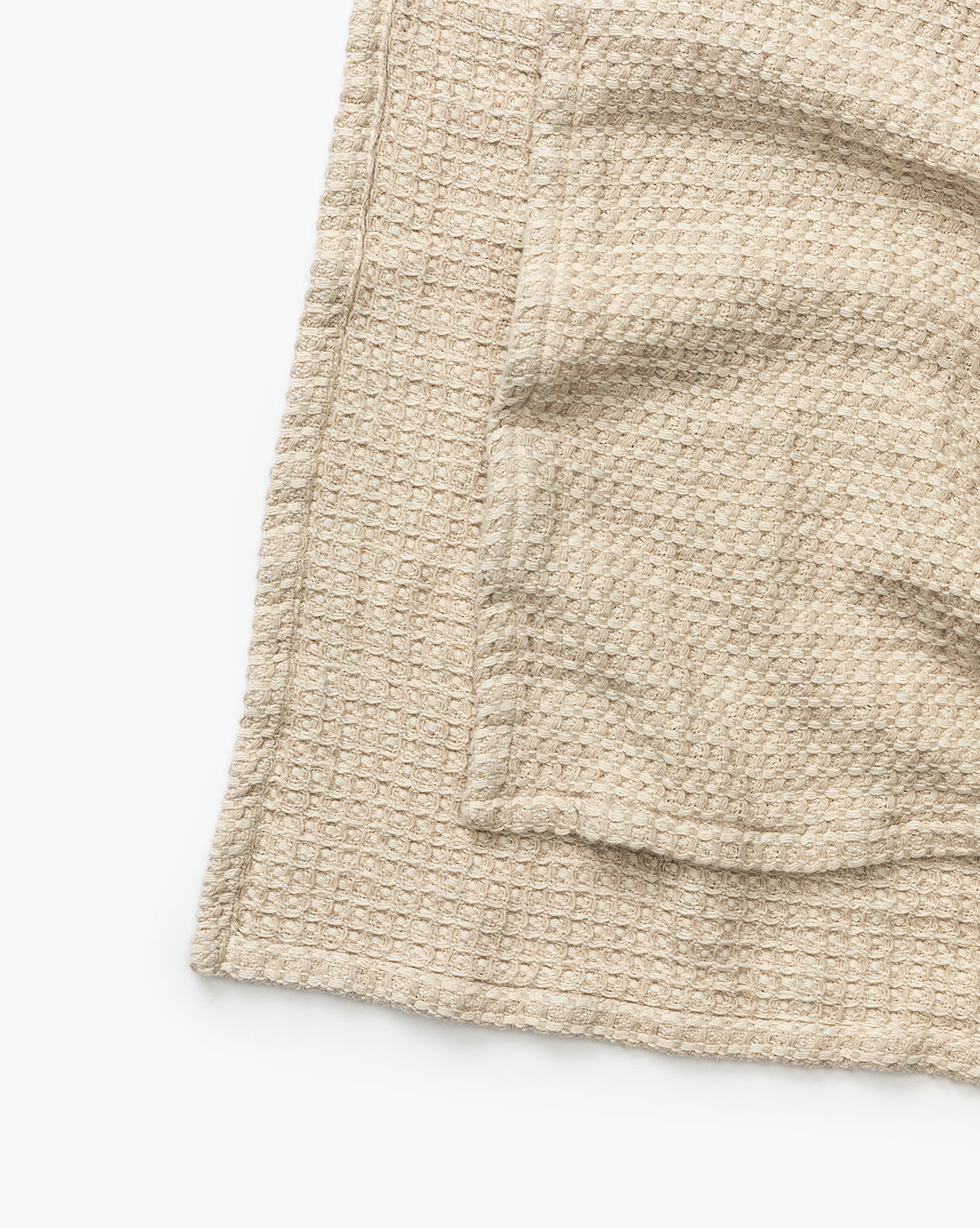 The Penedo Duffy Oversized Throw, featuring a beige textured waffle-knit cotton-hemp blend, is folded on a white surface with only part of the throw visible in the image. McGee & Co.