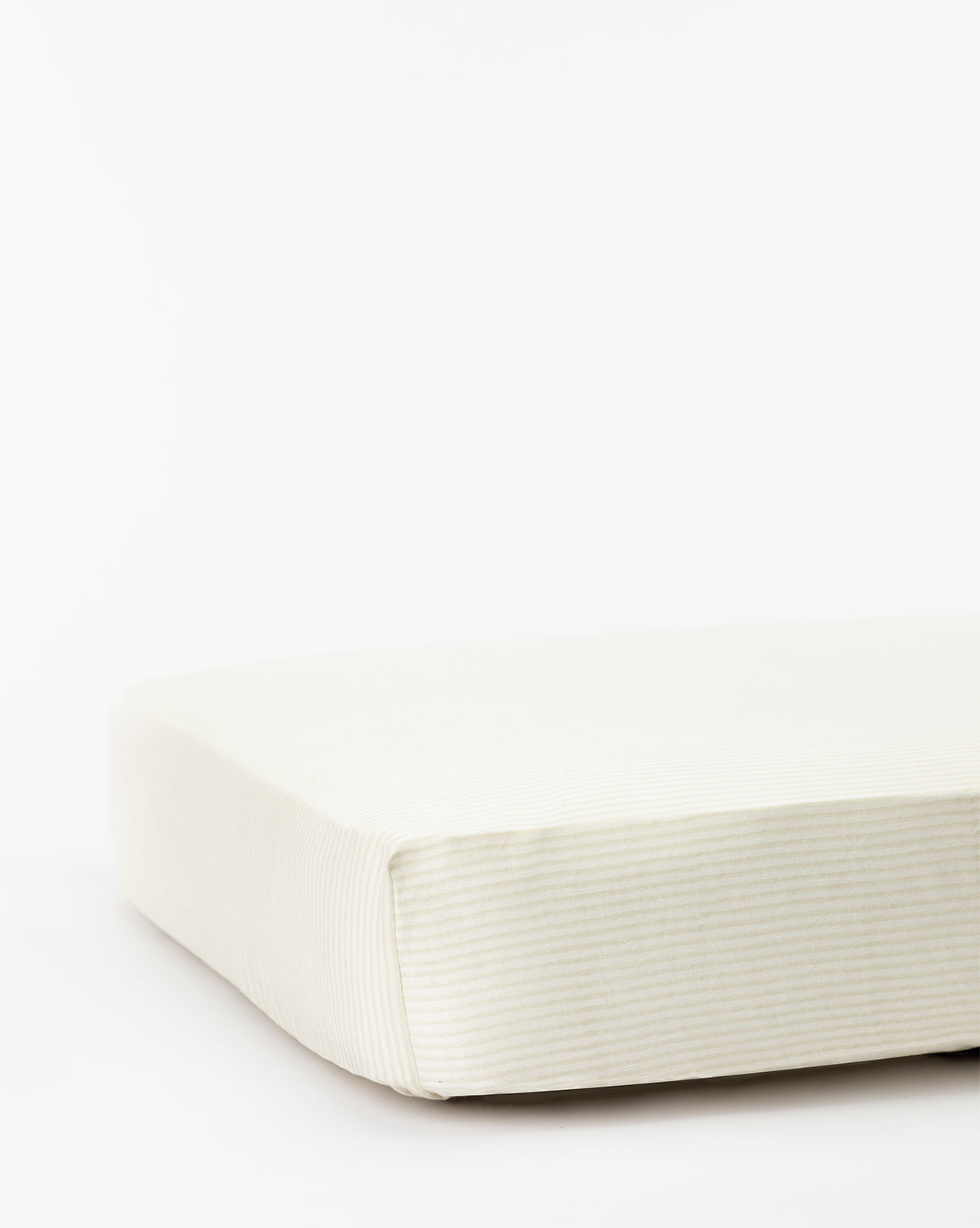 A close-up of a cream-colored, subtly striped mattress or cushion pairs perfectly with the Easton Crib Sheet or other crib bedding, creating a cozy look for your babys room against a white background.