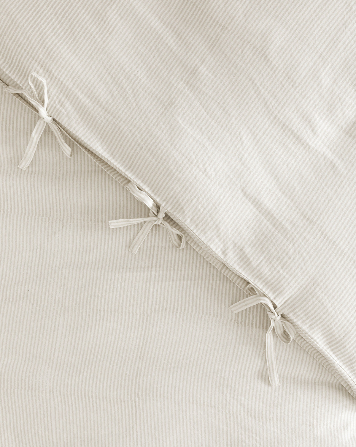A close-up of the Easton Striped Duvet Cover in soft cream and oatmeal, featuring three fabric ties that secure two layers. Its subtle pattern and texture create elegant bedding with an invitingly soft feel.