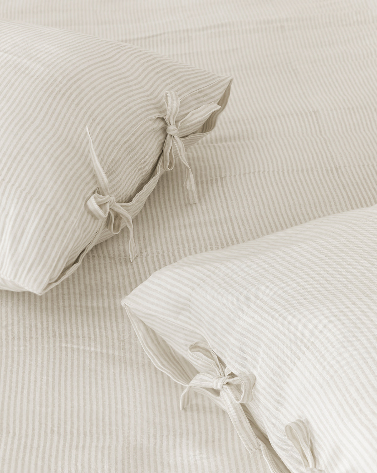 Two cream-colored Easton Striped Shams (Set of 2) with subtle beige stripes and fabric ties rest on a matching bedspread, giving any bedroom a cozy, minimal look.
