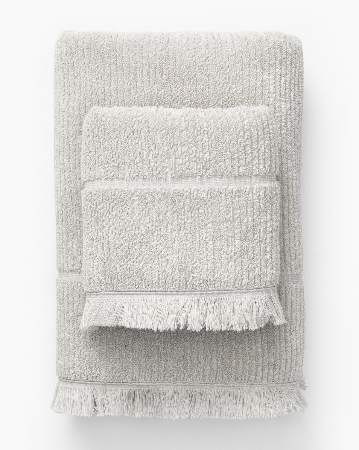 Two light gray ribbed cotton towels with textured surfaces and fringed edges, stacked against a white background, from the Edessa Bath Collection.