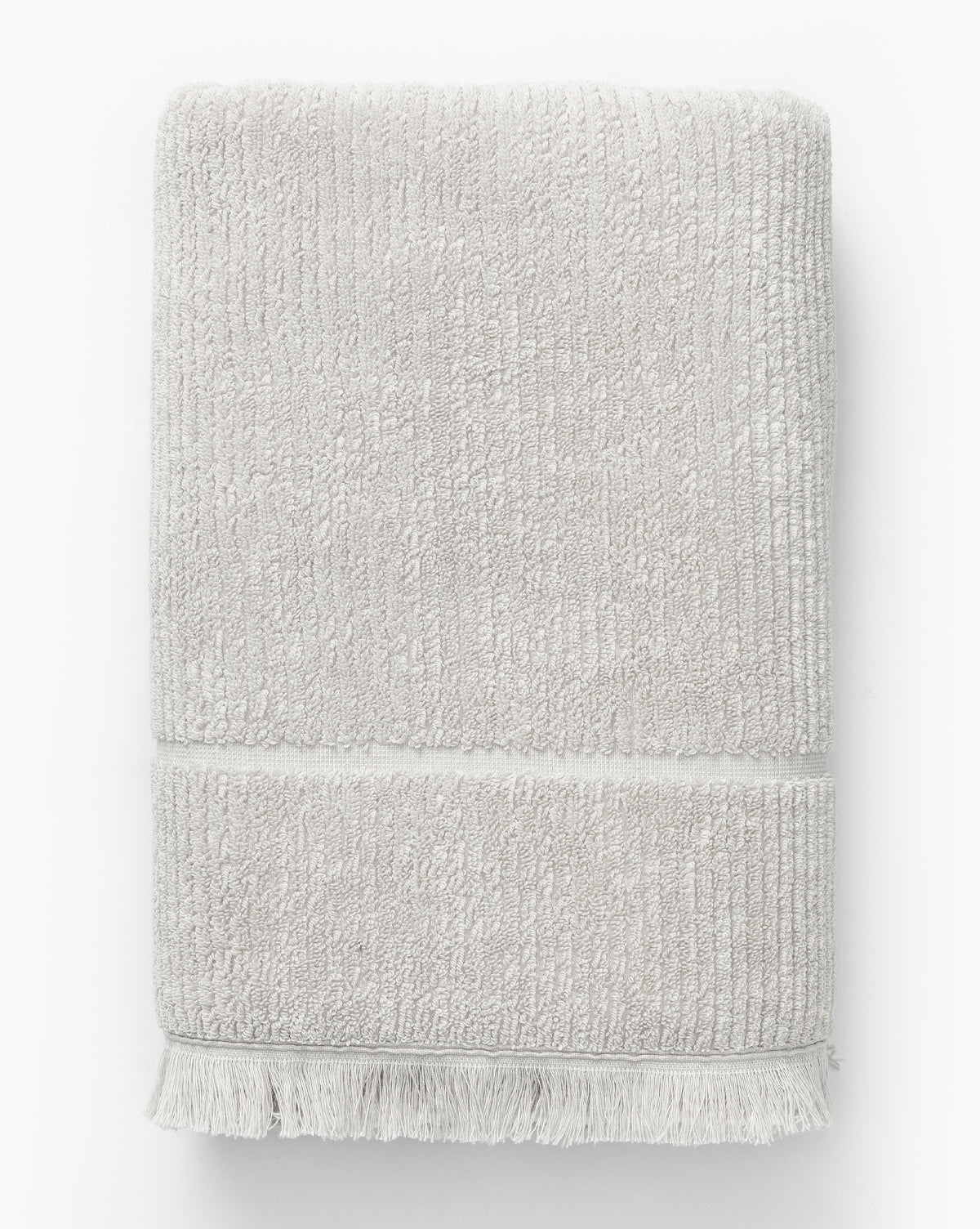 A light gray ribbed cotton towel with fringed edges from the Edessa Bath Collection is neatly folded and displayed on a white background.