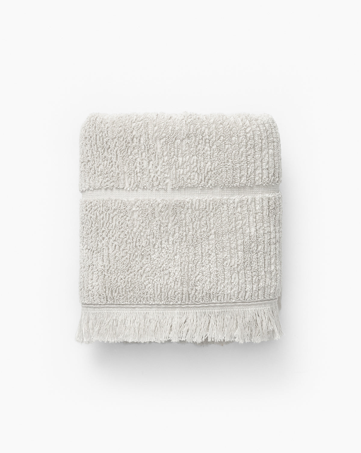 A light gray, ribbed cotton towel with a fringed edge from the Edessa Bath Collection is neatly folded and displayed on a white background.